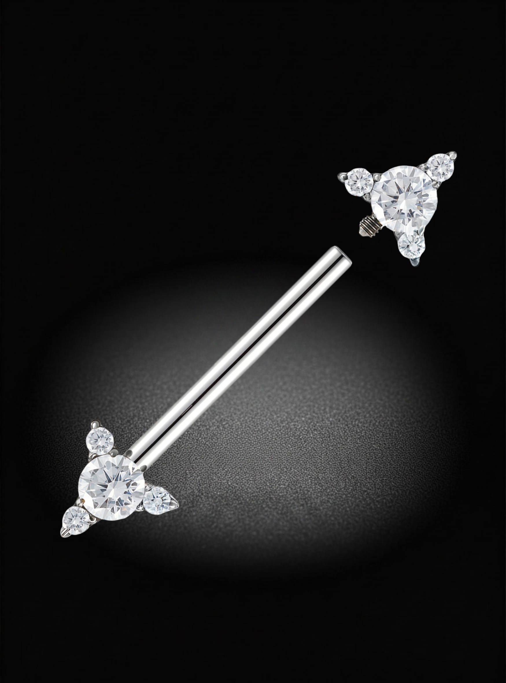 A titanium nipple internally threaded barbell with three clear gemstones on each end, displayed diagonally against a dark black background with a soft spotlight effect.