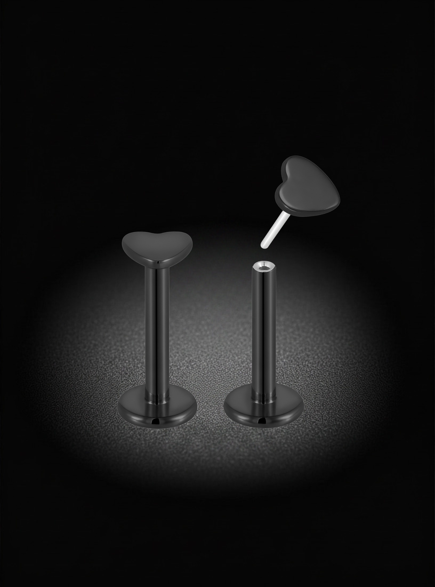 Two black titanium body jewelry piercings with heart-shaped tops, shown on a black background with a spotlight effect. One piece is upright, and the other is shown with its flat heart end flipped up.