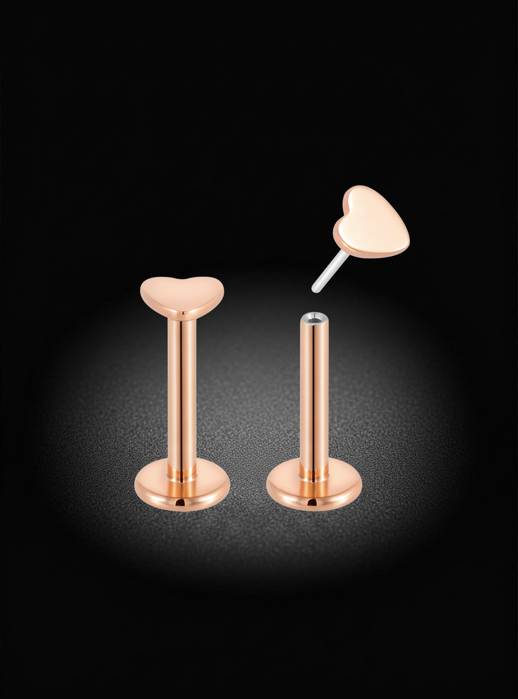 Rose gold flat-back labret ear piercings with heart-shaped studs, shown on a black background with one earring assembled and the other disassembled to show the post and backing.