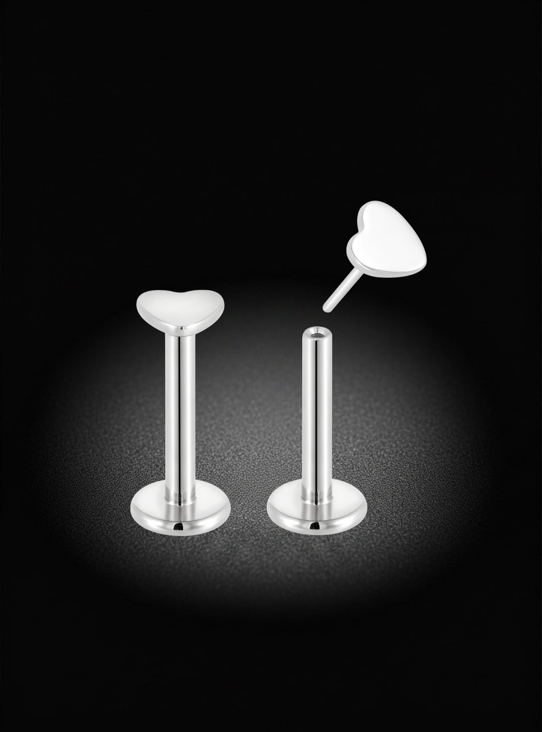 Two silver-toned labret earrings with heart-shaped tops, shown on a black background with one earring upright and the other lying on its side to display the back.