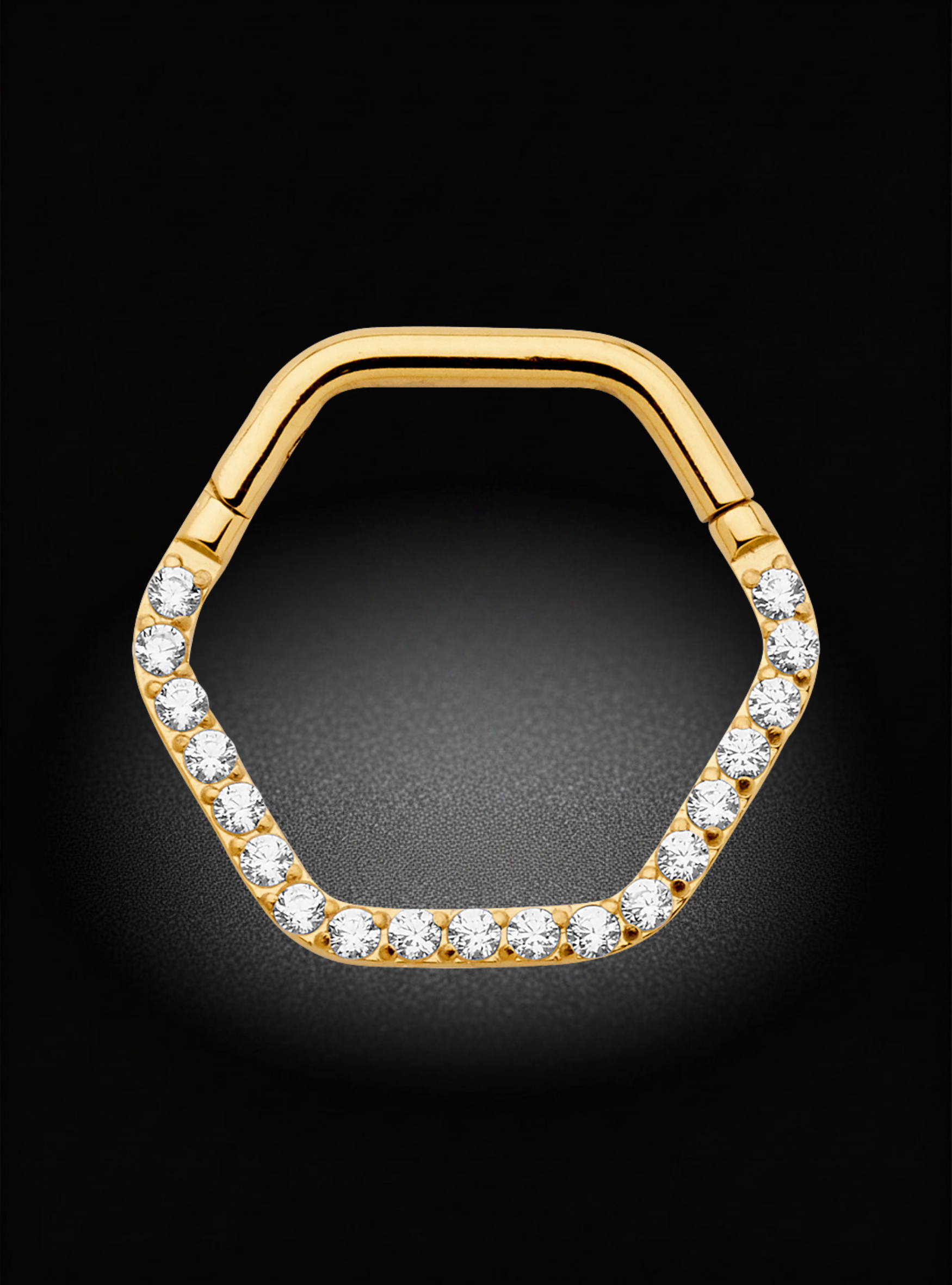 A gold hexagonal ring with clear gemstones set along the front edge, displayed on a dark black background.