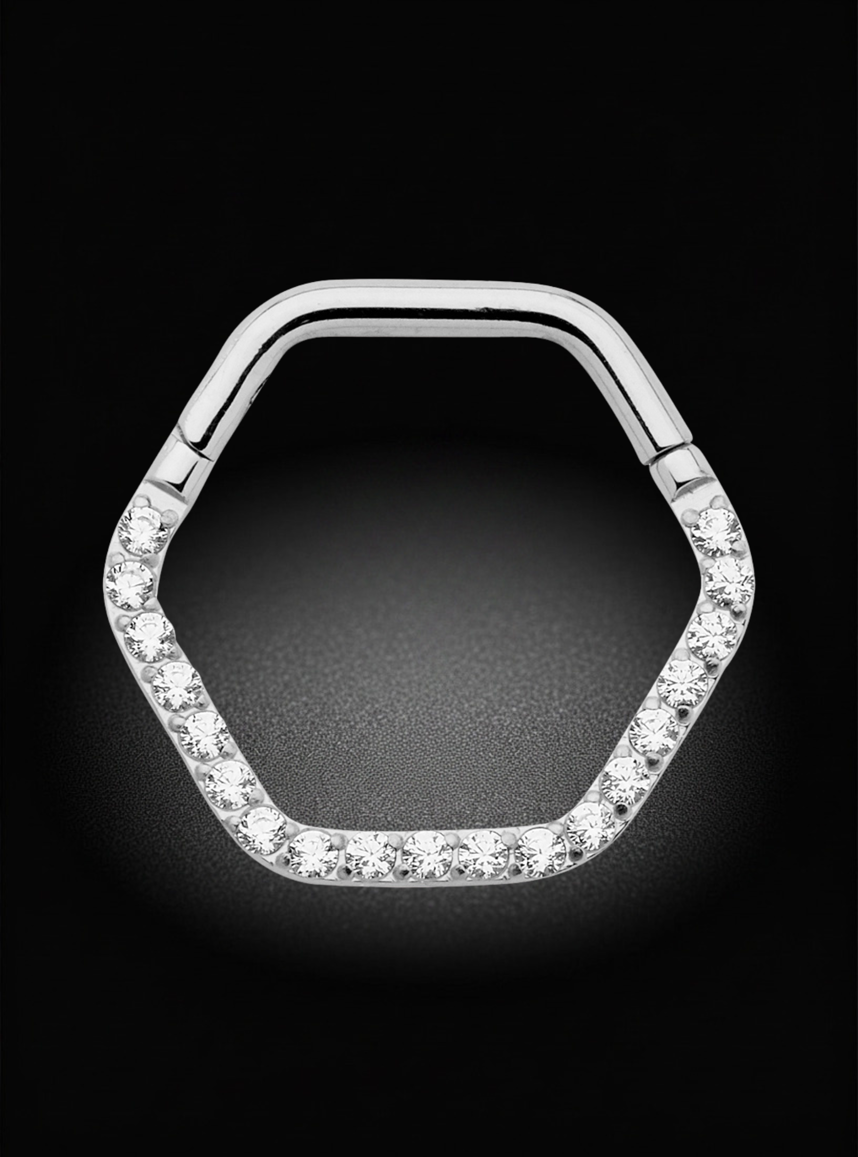A silver-toned hexagonal ring with clear gemstones set along the lower three sides, photographed against a black background.
