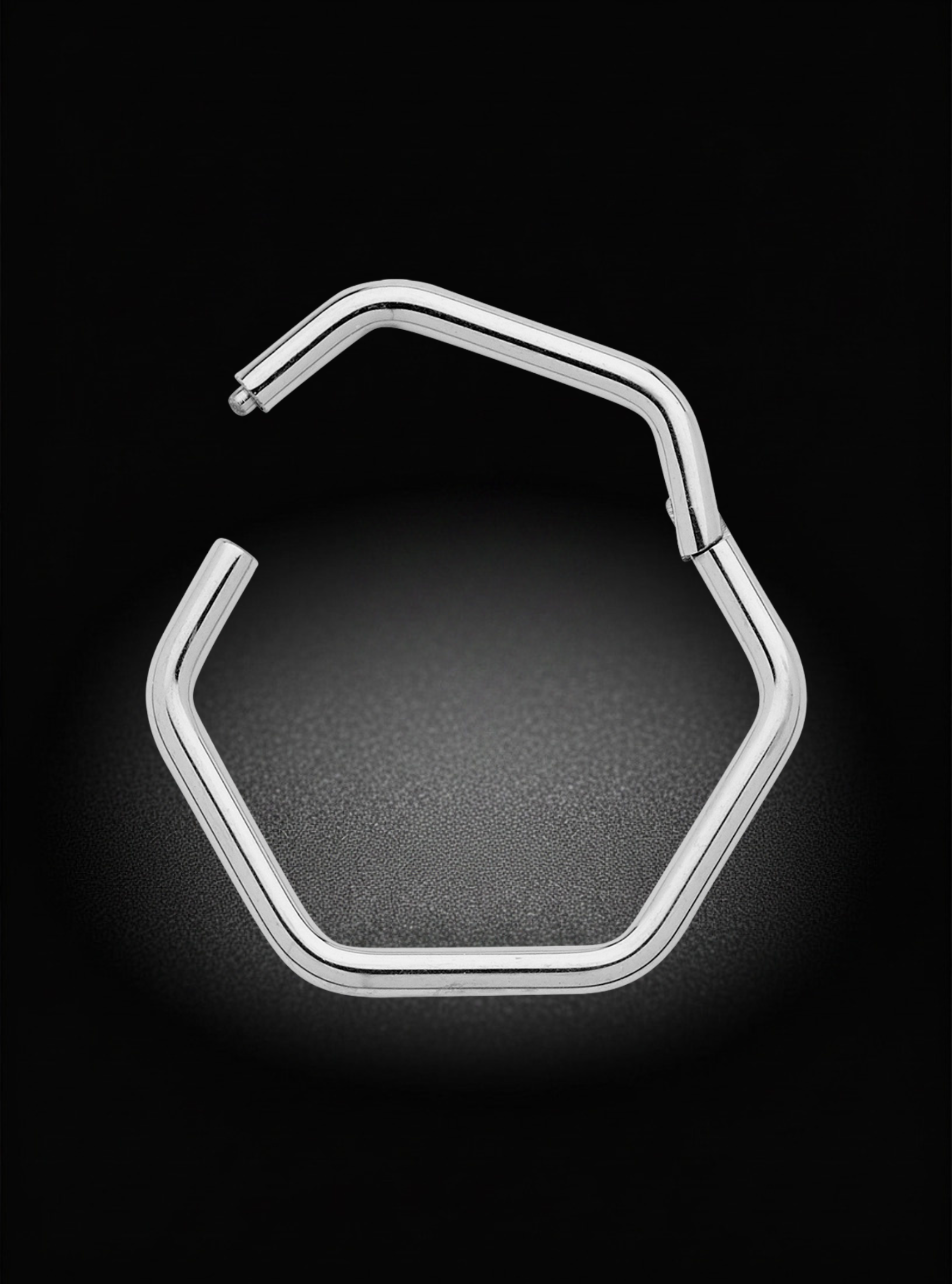 A silver-toned metal hexagonal hoop earring with an open back, shown on a dark black background with a soft glow.