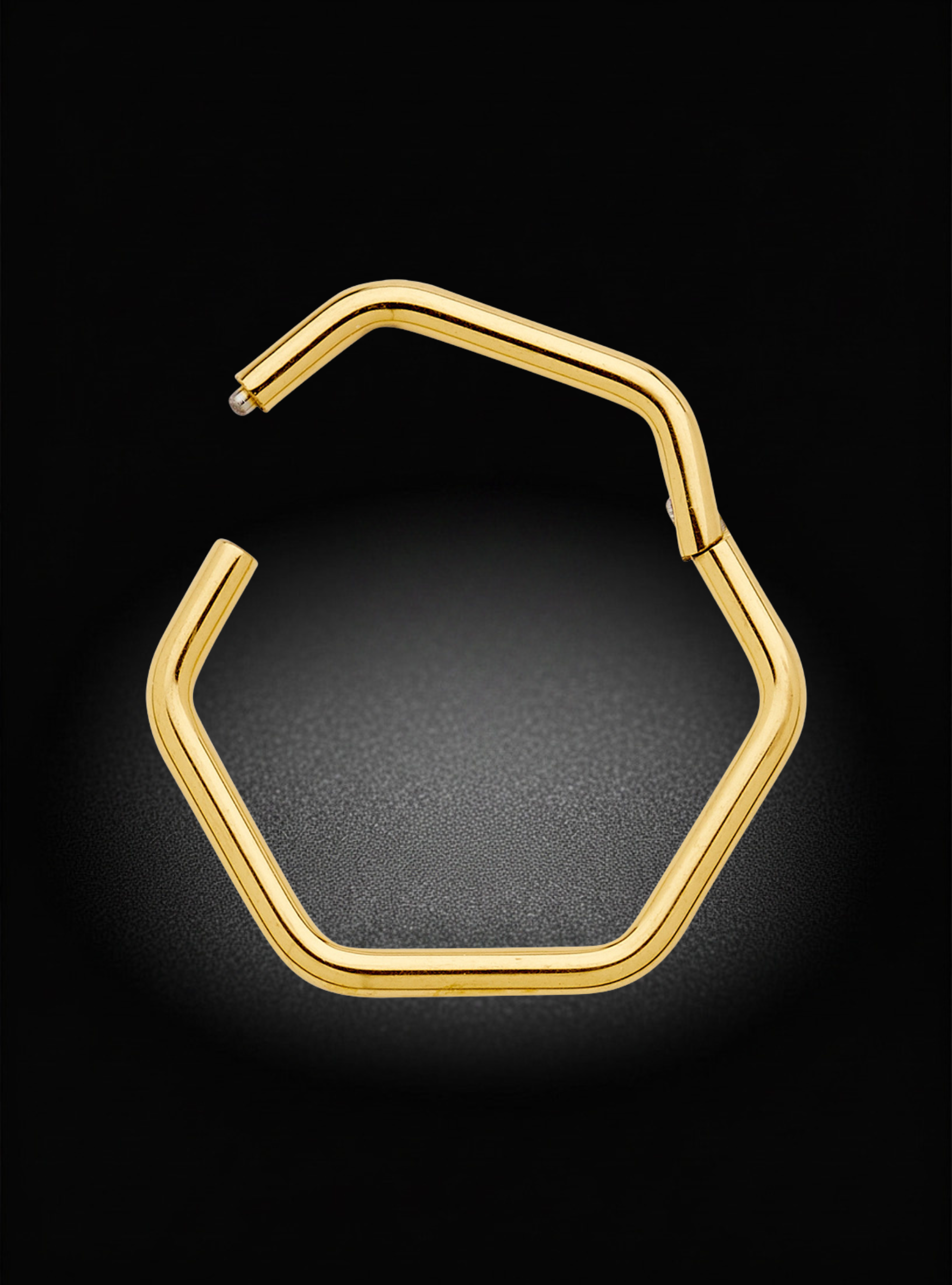 A gold-toned hexagonal open hoop earring, shown on a dark textured background with a soft spotlight effect.