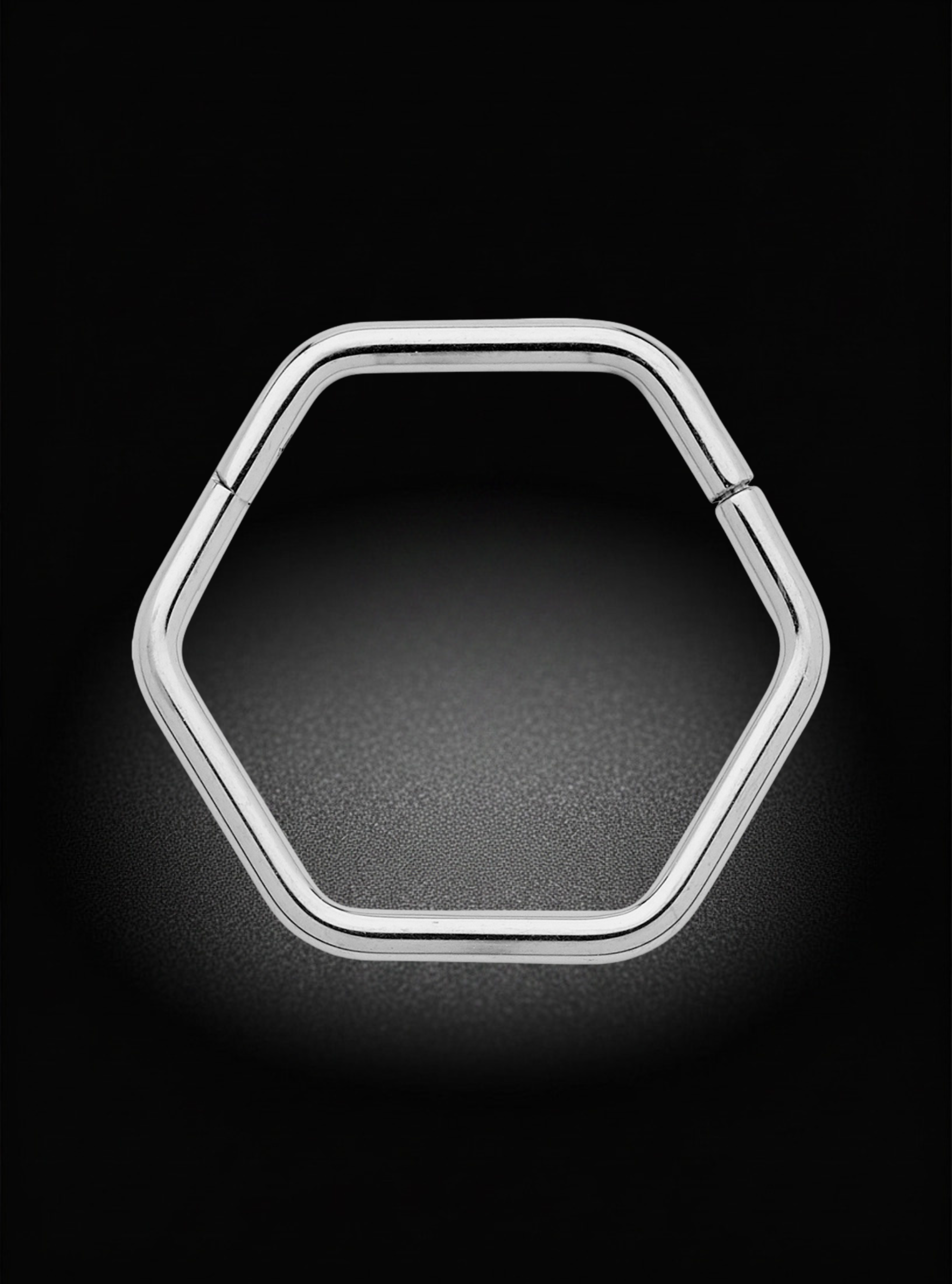 A silver-toned hexagonal metal ring with a polished finish, shown on a dark black background with a soft glow.