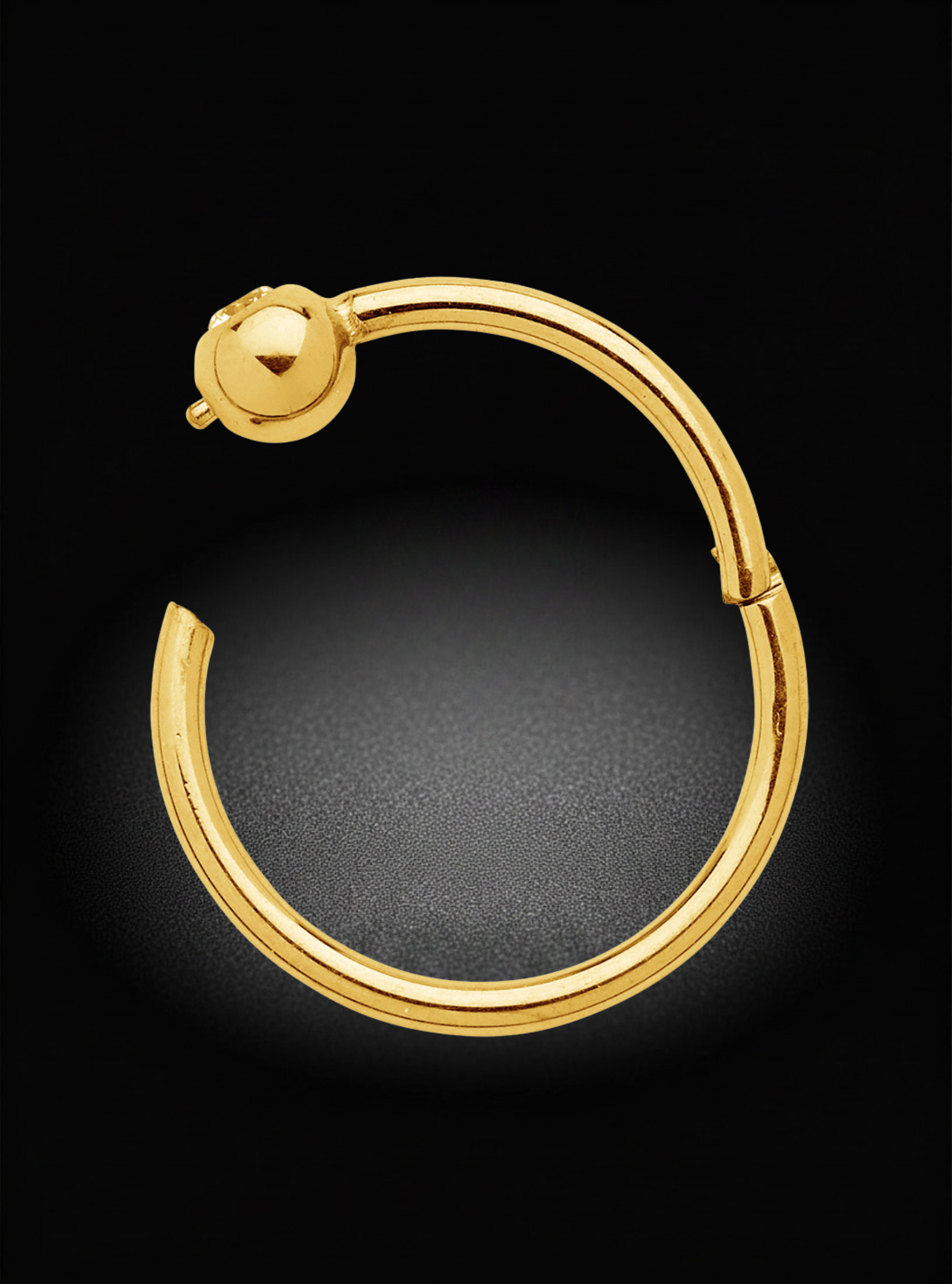 A polished gold huggie hoop earring with a ball stud closure, displayed on a dark textured background.