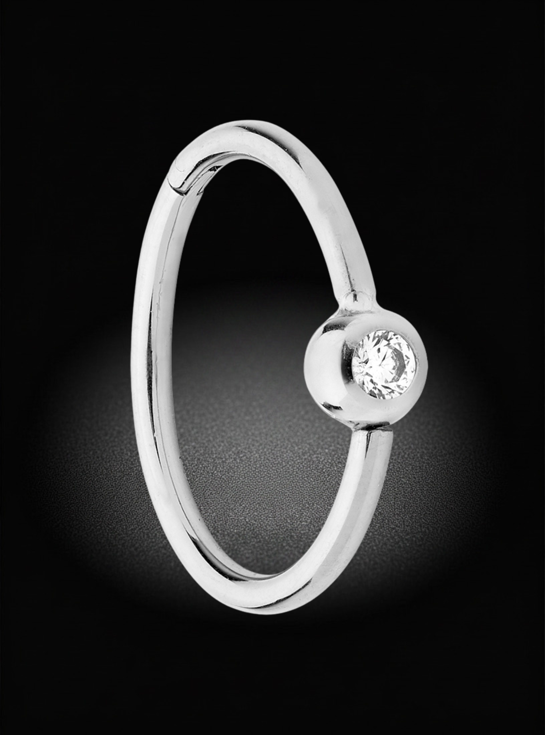 A polished silver-toned ring with a small round bezel-set clear gemstone, shown on a black background.