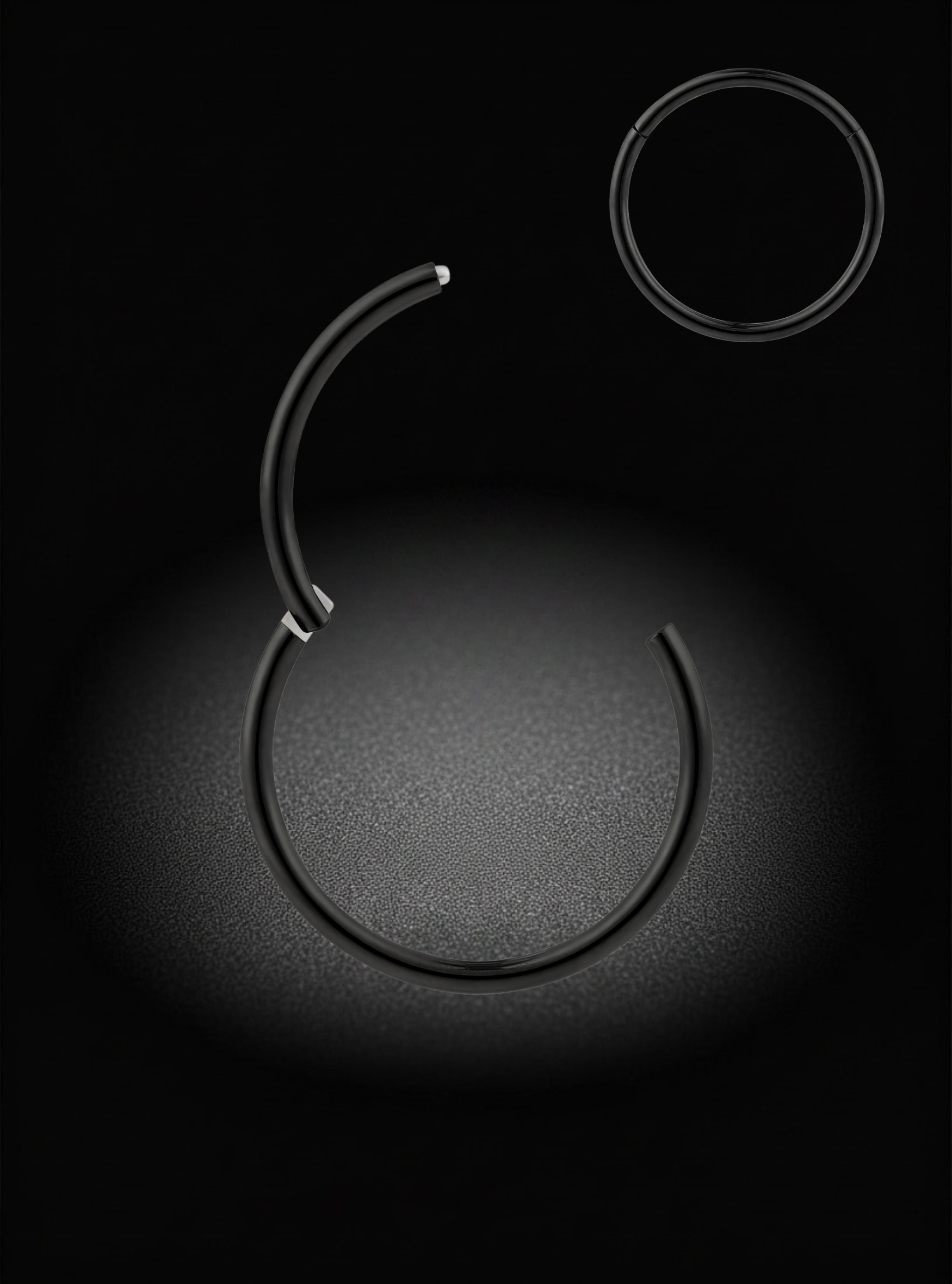 A pair of thin black metal hoop earrings, one of which is shown open and suspended against a dark spotlighted background, with a second earring shown flat in the upper right.