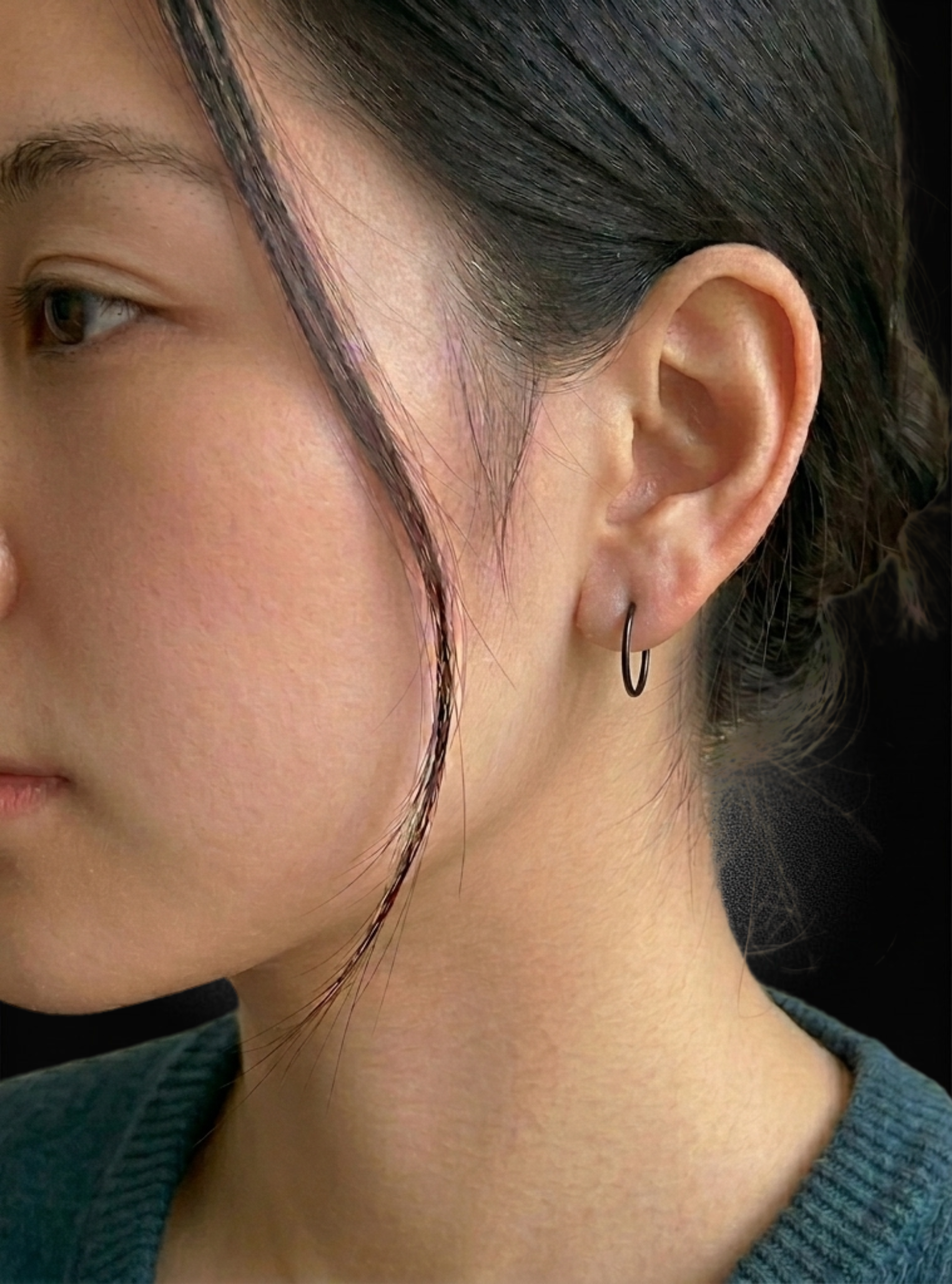 Close-up side profile of a woman wearing a small black hoop earring.