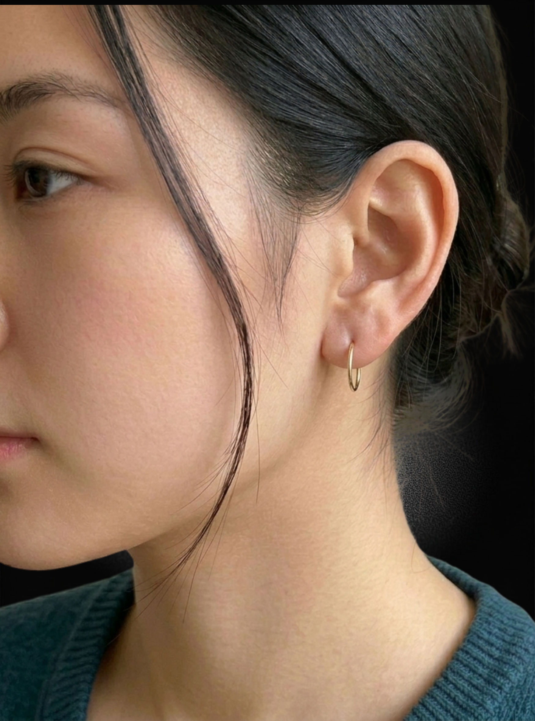 A close-up side profile of a woman wearing a delicate, small gold hoop earring on her earlobe.