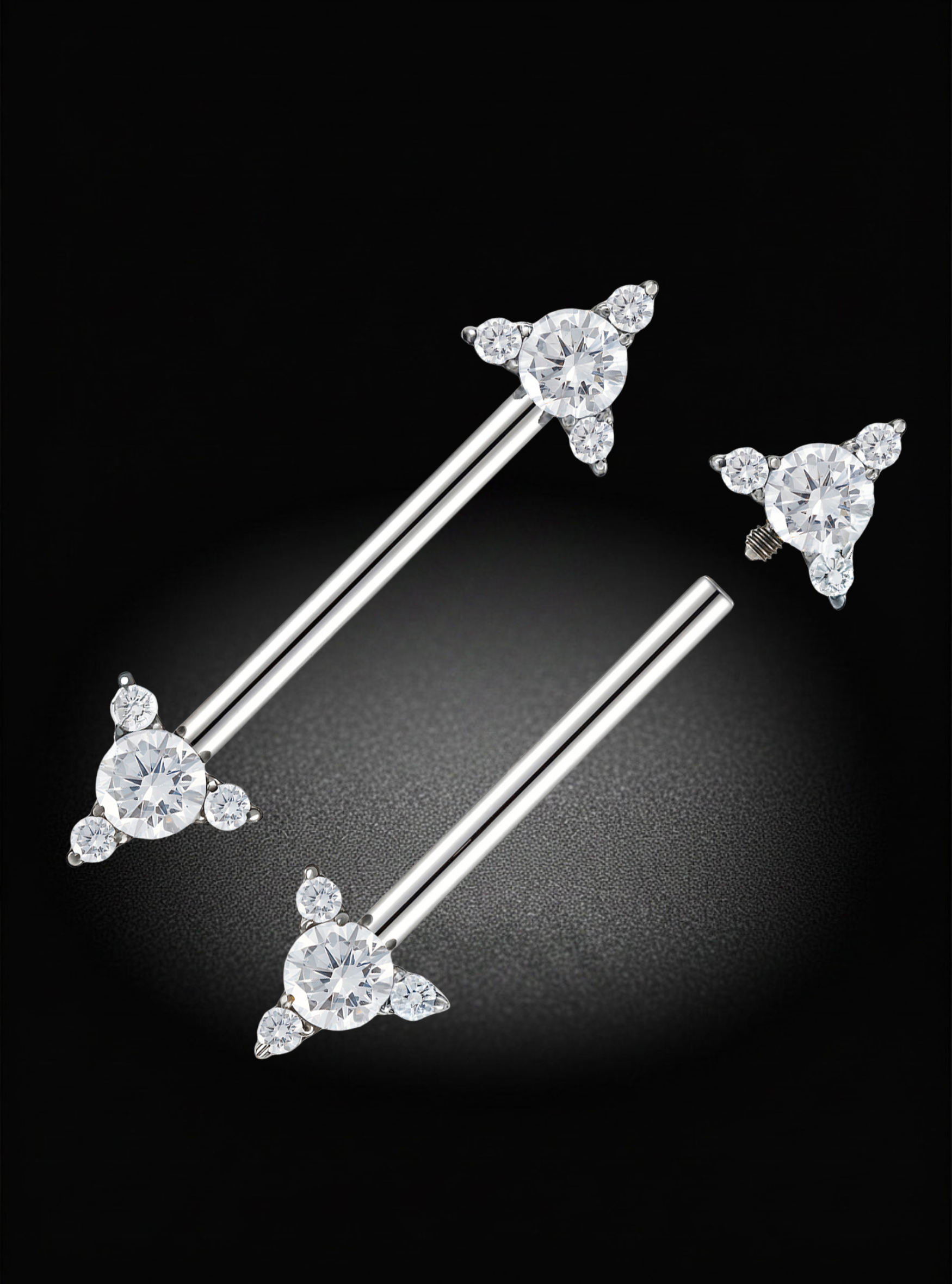 A pair of silver-toned barbell nipple barbells with triangular cluster settings set with clear gemstones, displayed on a black background.