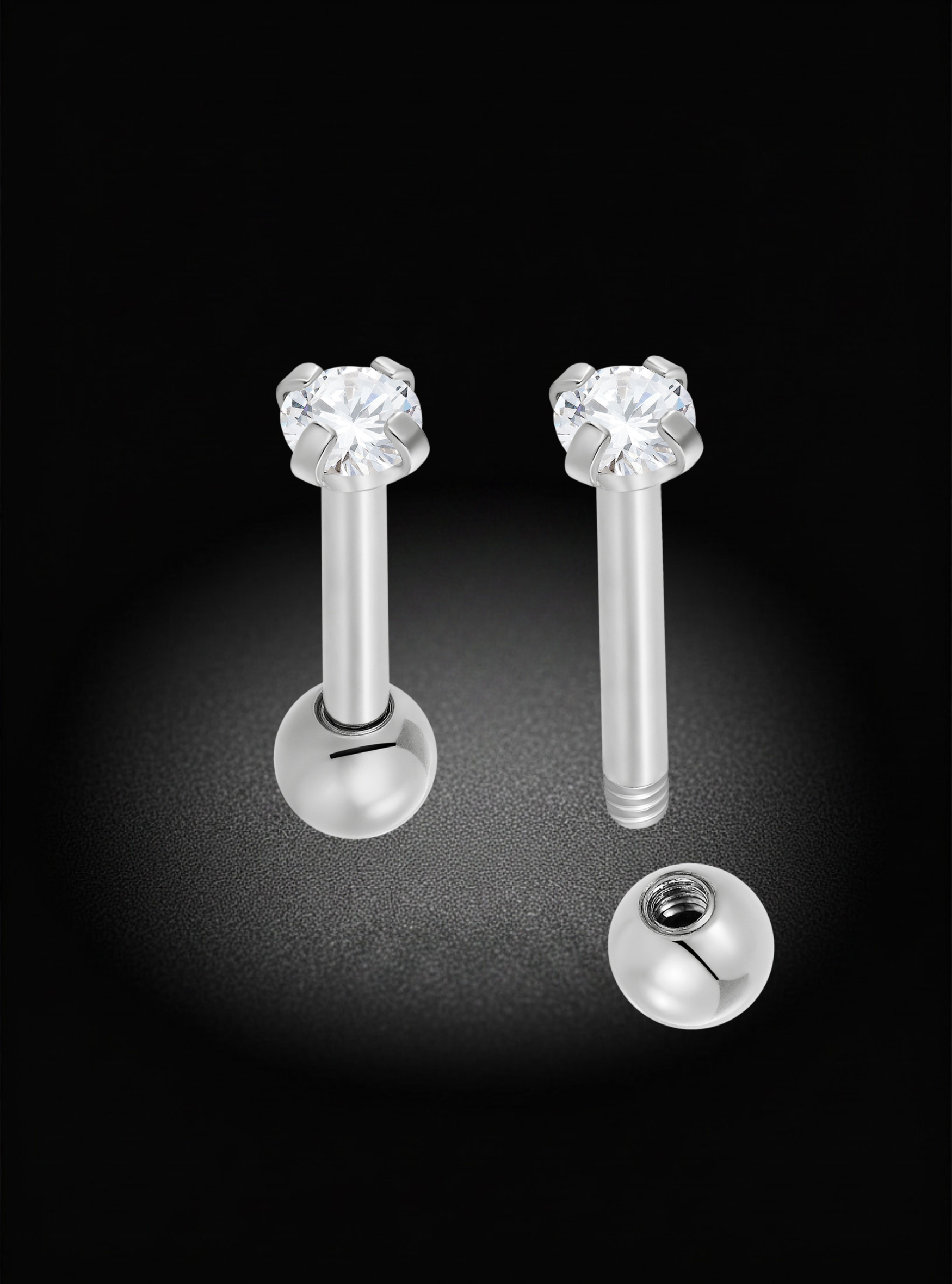 Two silver-toned labret piercing studs with clear faceted gemstones and ball backings, shown on a black background with one stud assembled and the other disassembled to show the back.