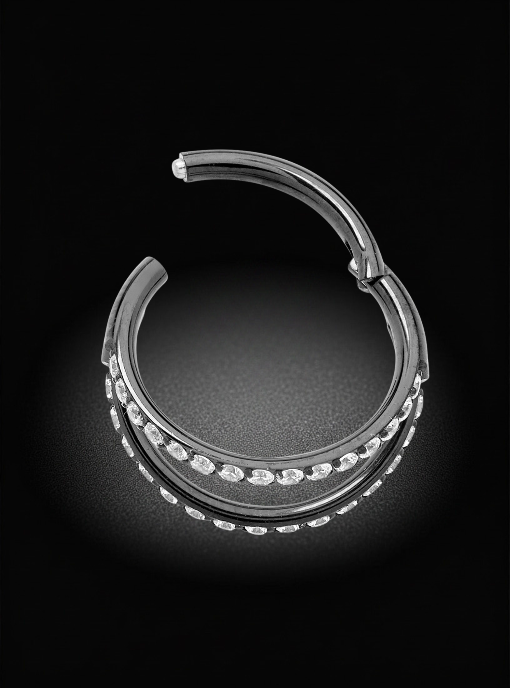 A polished black titanium hoop earring with rows of clear gemstones along the front, photographed on a dark black background with a soft spotlight effect.
