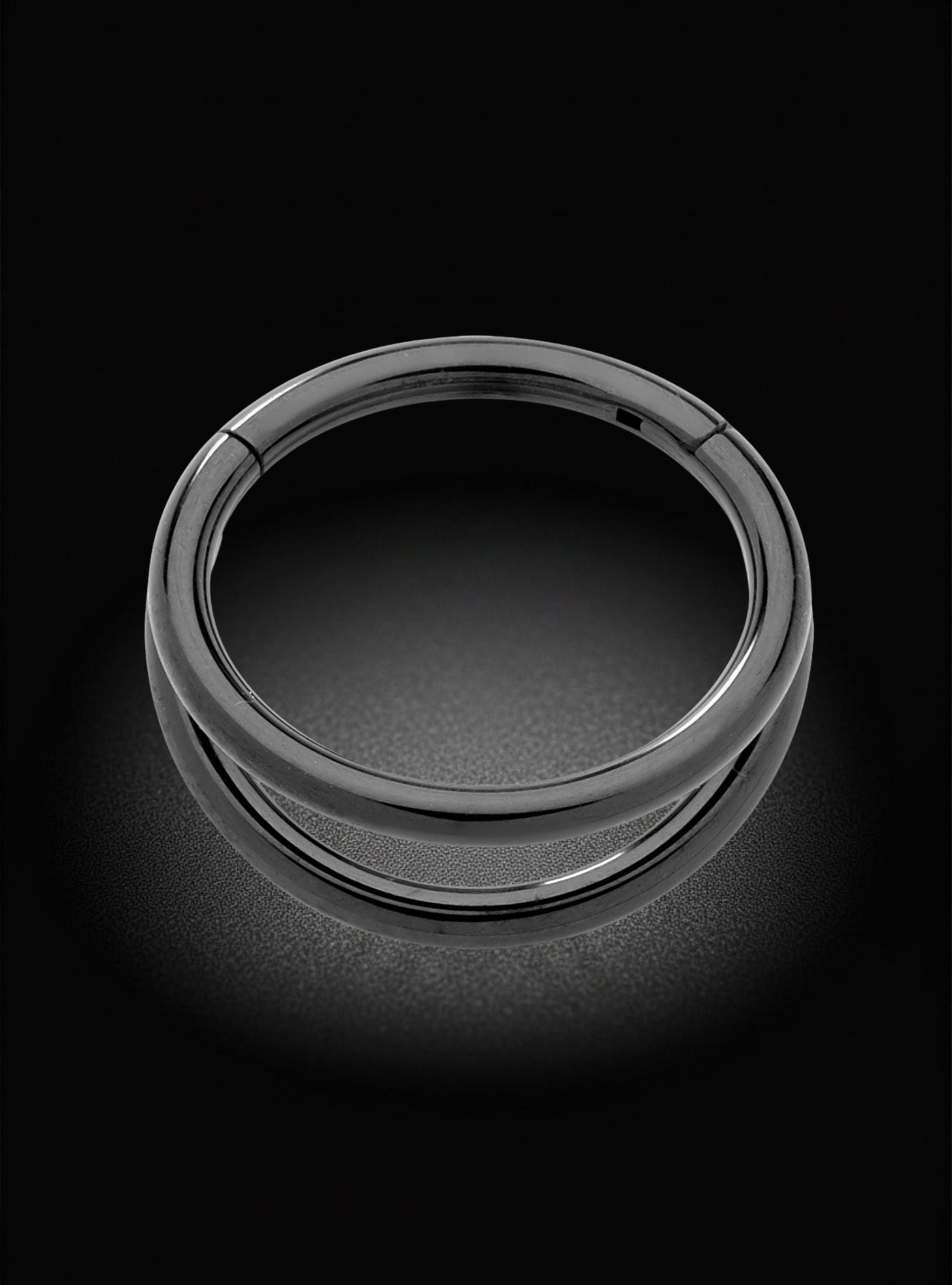 A polished silver-toned metal ring with a smooth, rounded profile, shown on a dark reflective surface against a black background.