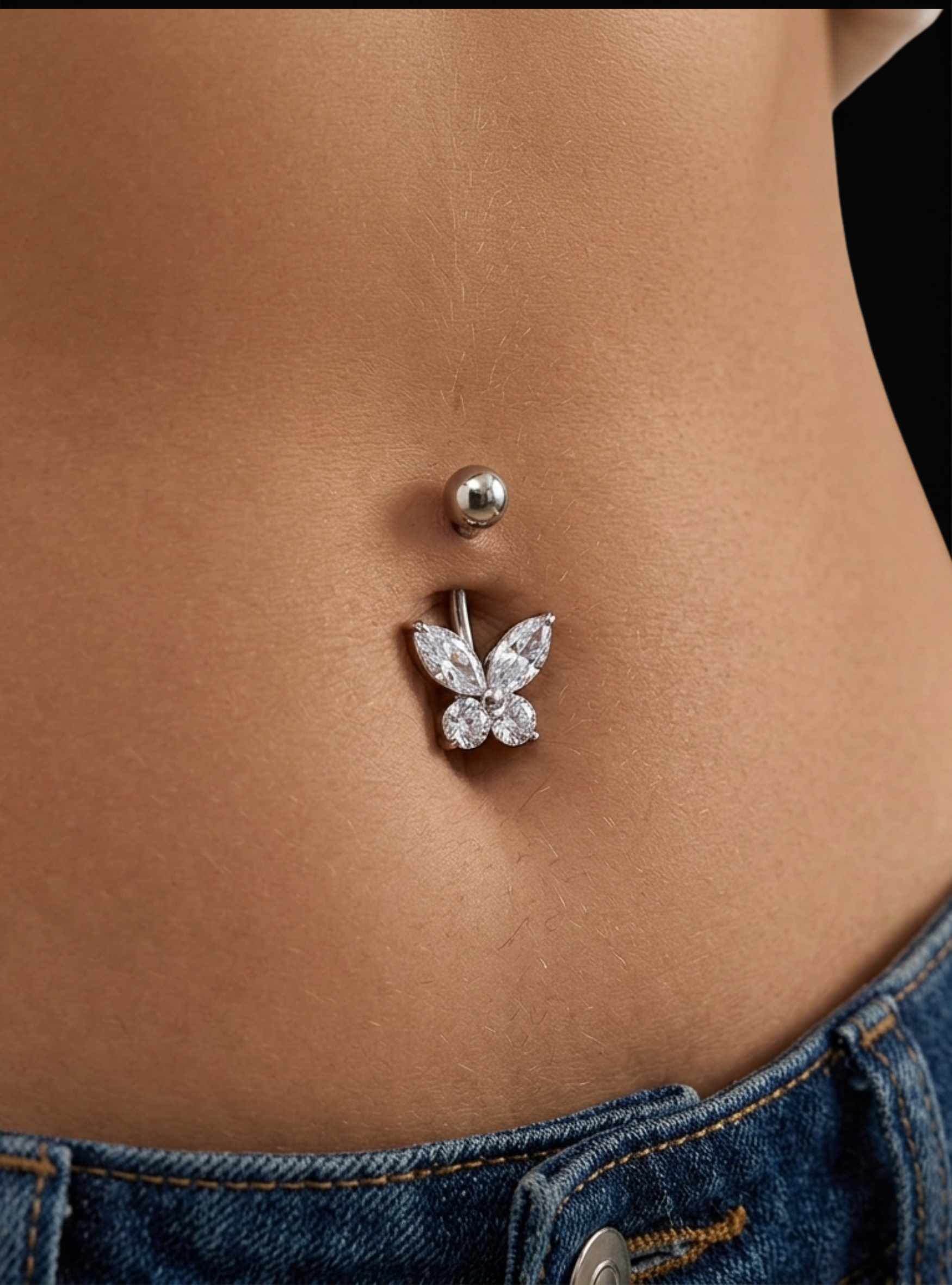 A close-up of a silver belly button ring with a butterfly-shaped crystal charm, worn on a model's navel above blue jeans.