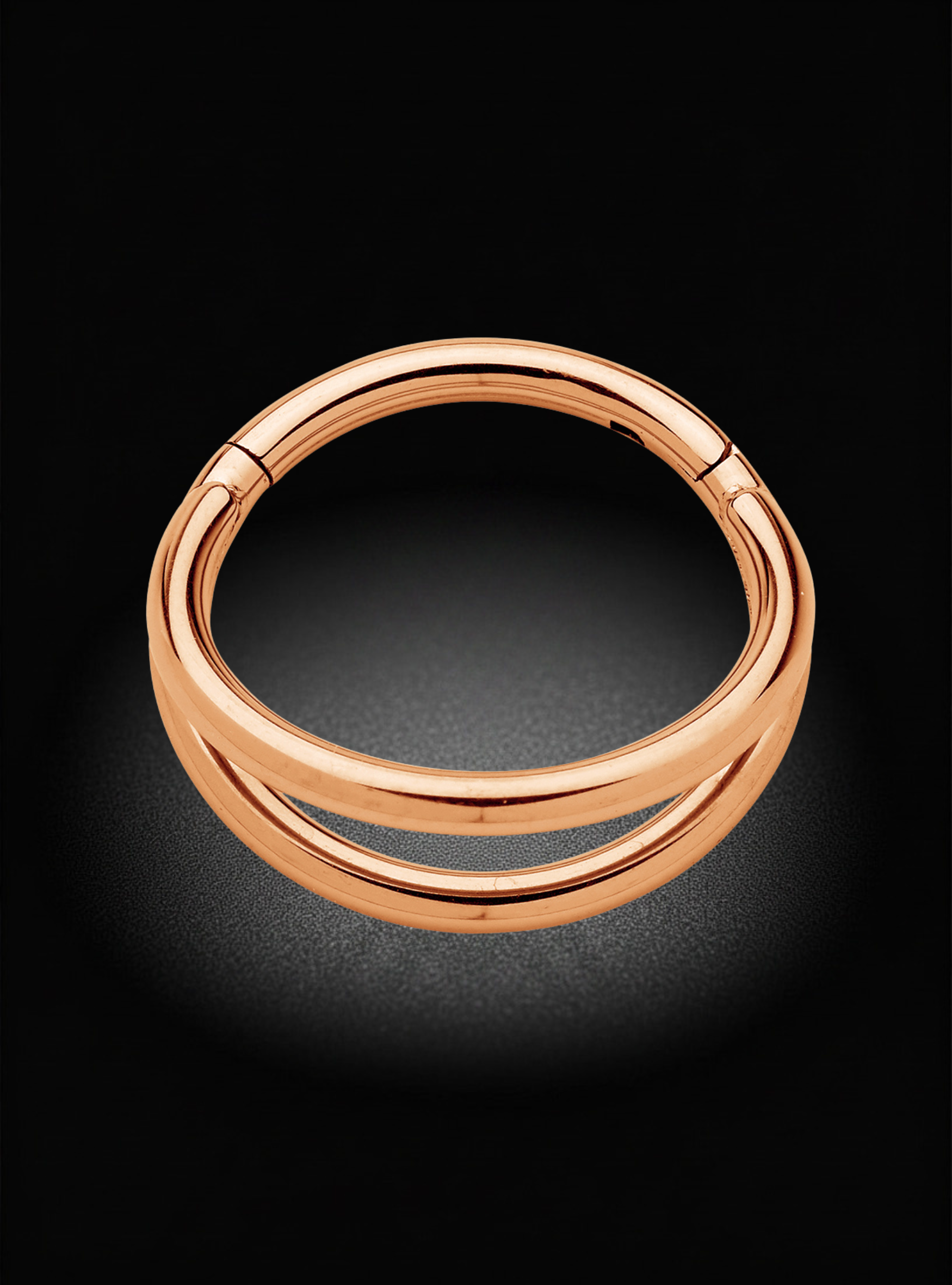 A polished rose gold double-band ring with a split clasp design, shown on a dark black background with a soft spotlight effect.