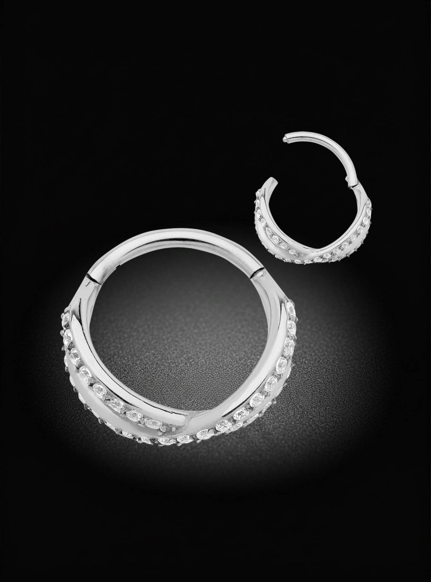 A pair of silver hoop earrings adorned with small clear stones, displayed on a dark black background.