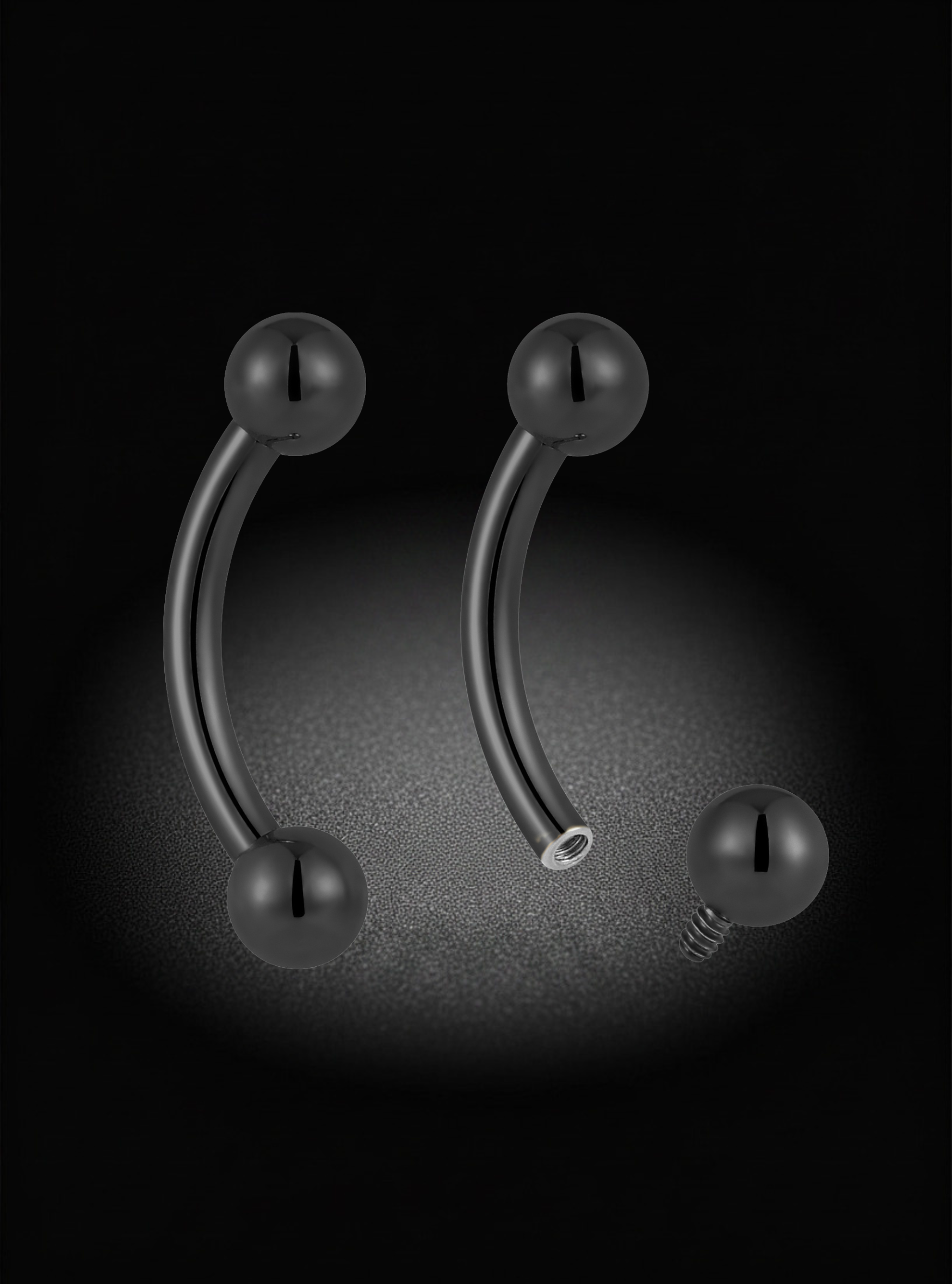 Two curved barbell piercings with spherical ball ends and a separate screw-back disc, shown on a black background with a soft spotlight effect.