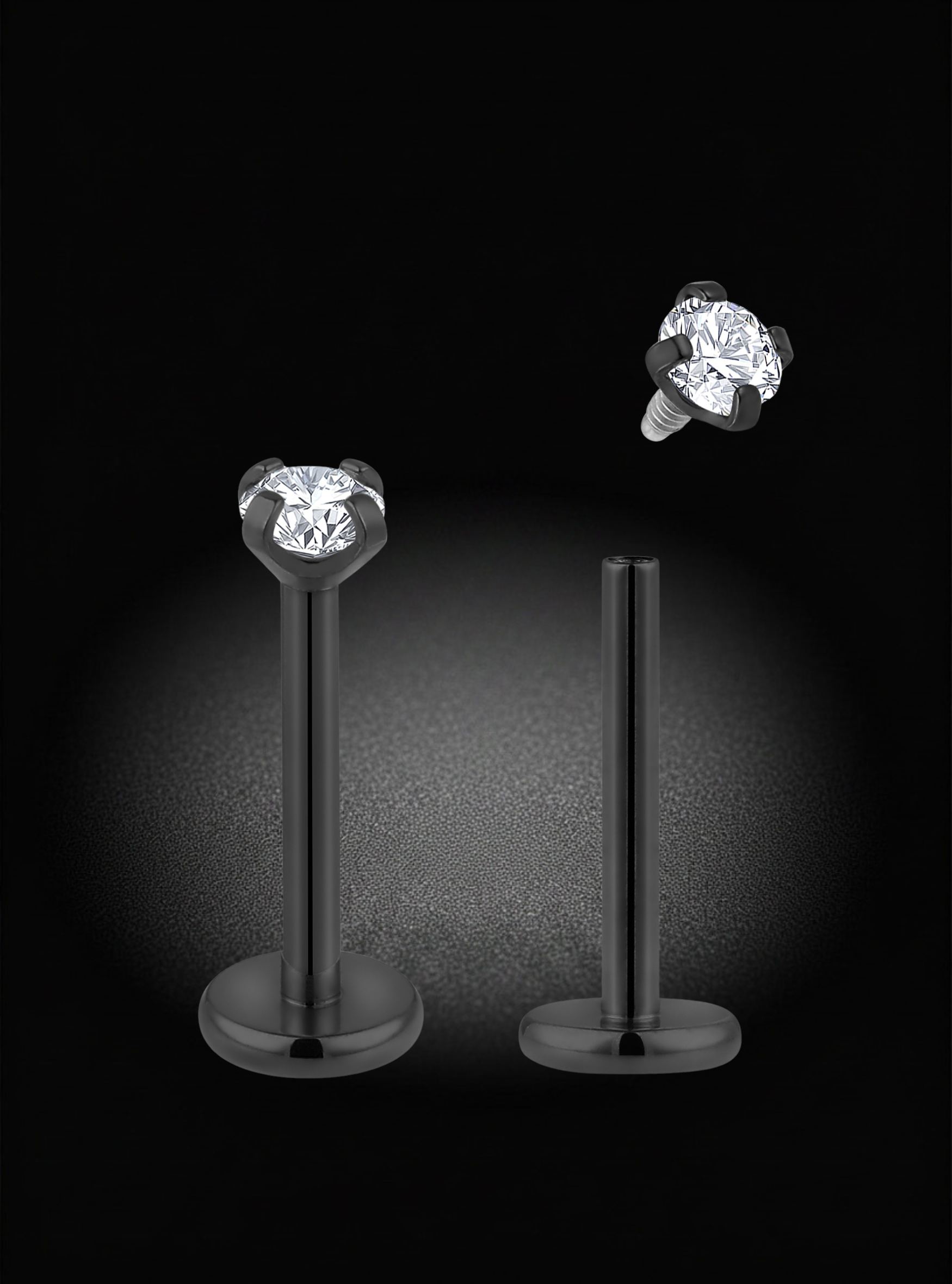 A pair of silver-toned labret ear piercings with round brilliant-cut clear gemstones, displayed on a black background with one piece shown upright and the other floating to demonstrate the post and butterfly back.