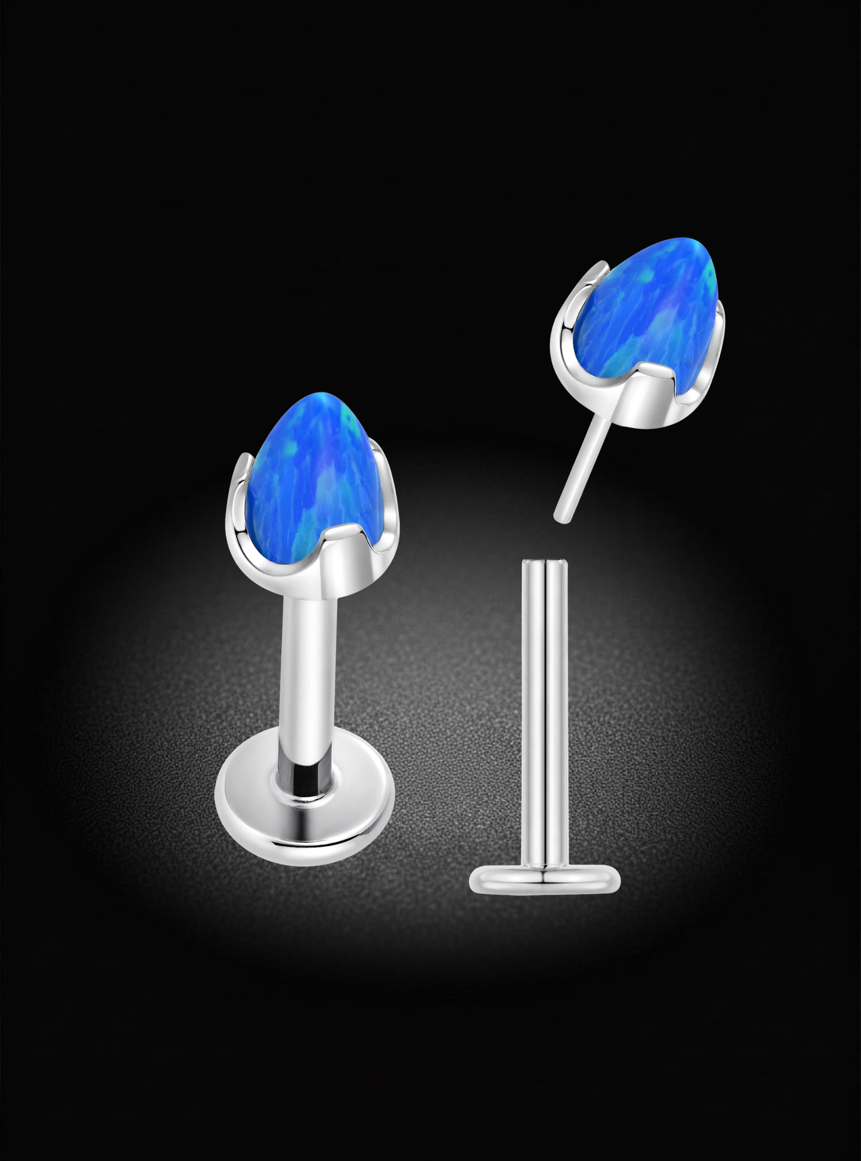 A pair of silver-toned labret studs with teardrop-shaped blue gemstones, shown on a black background with one stud assembled and the other broken into its post and flat back components.