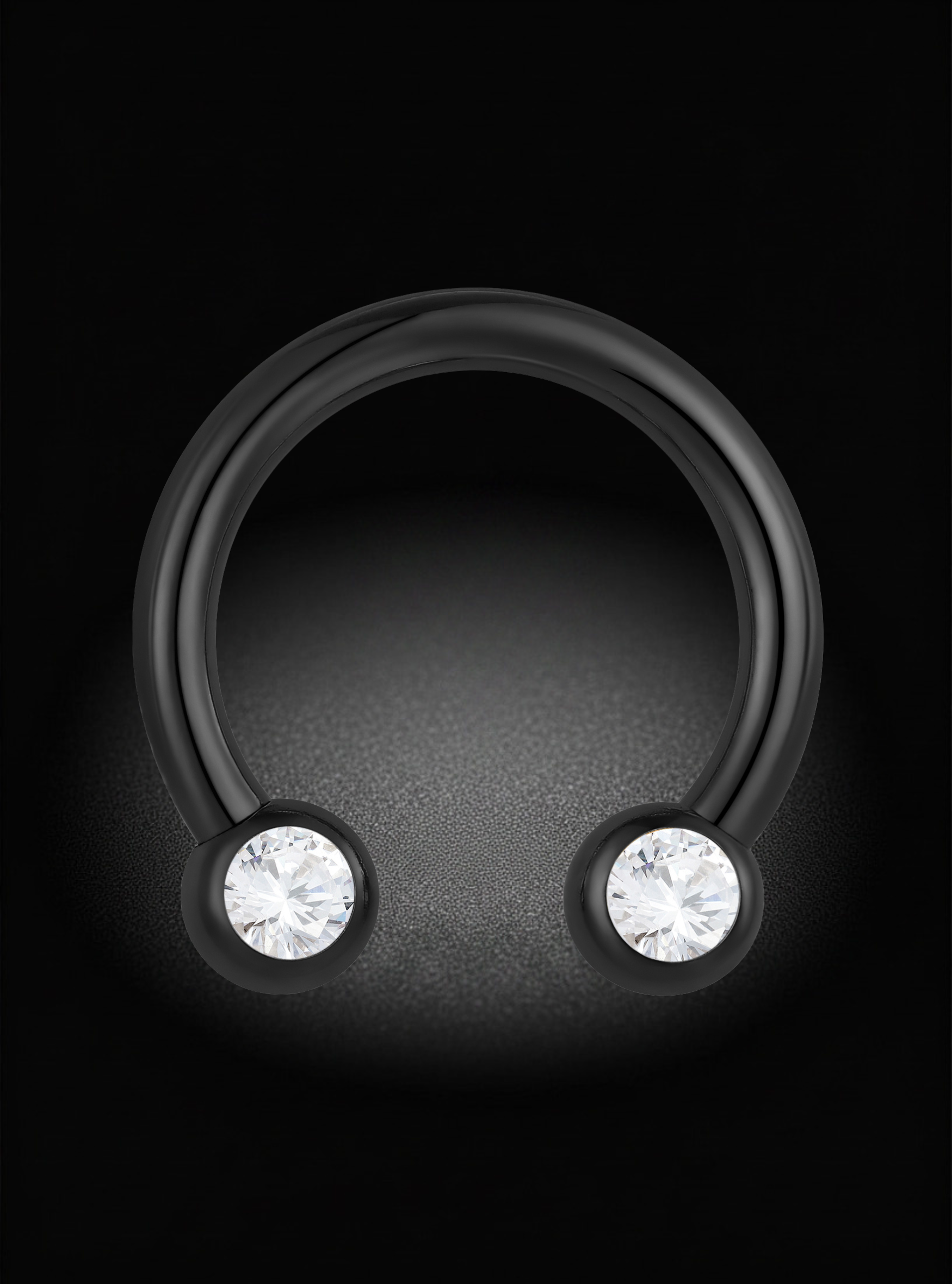 A matte black curved ring with two round bezel-set clear gemstones, shown on a dark textured background.