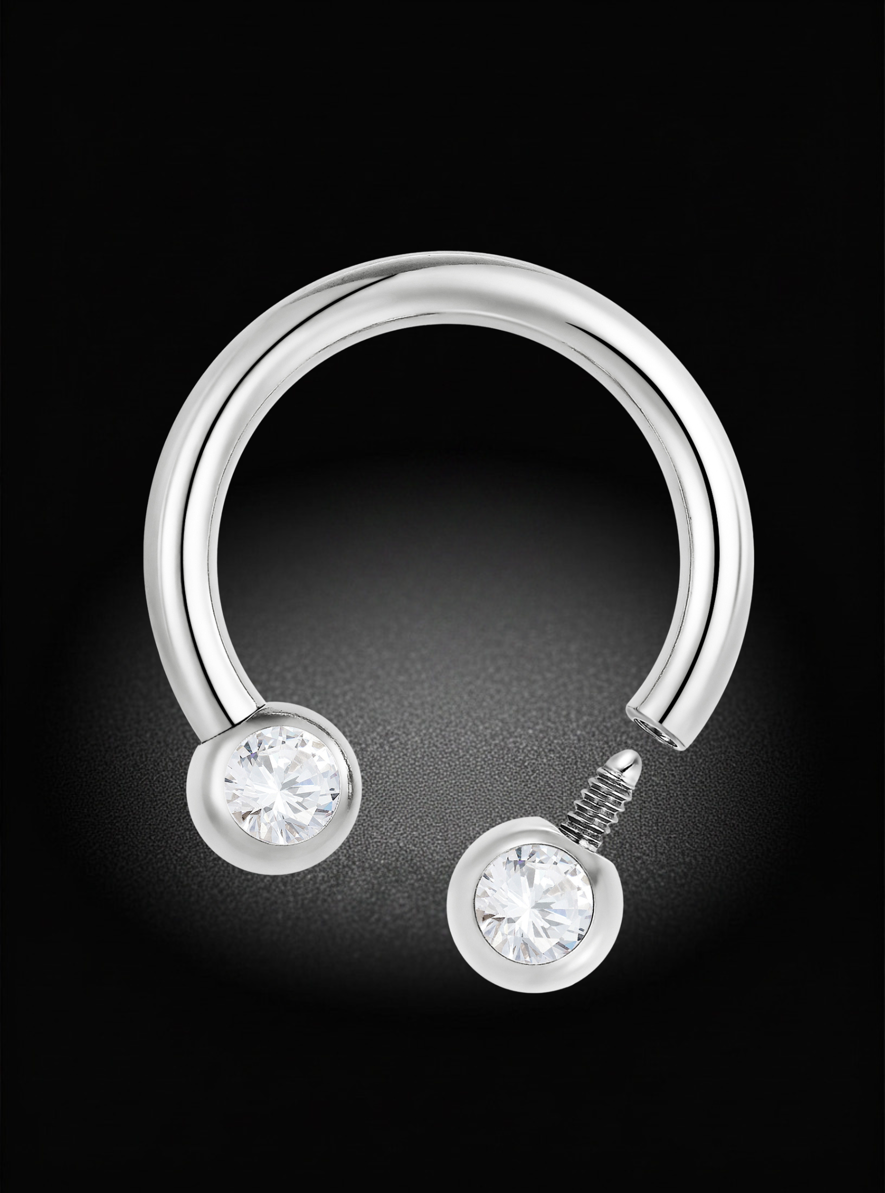 A silver-toned curved hoop earring with two bezel-set clear round gemstones, shown on a black background.