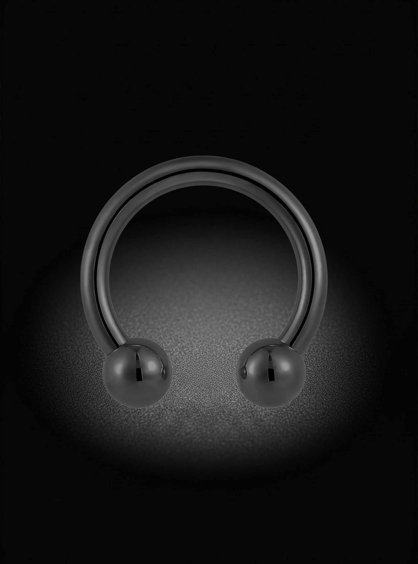 A black metallic labret piercing ring with a smooth, polished finish and a ball-shaped end, shown against a dark background with a spotlight effect.
