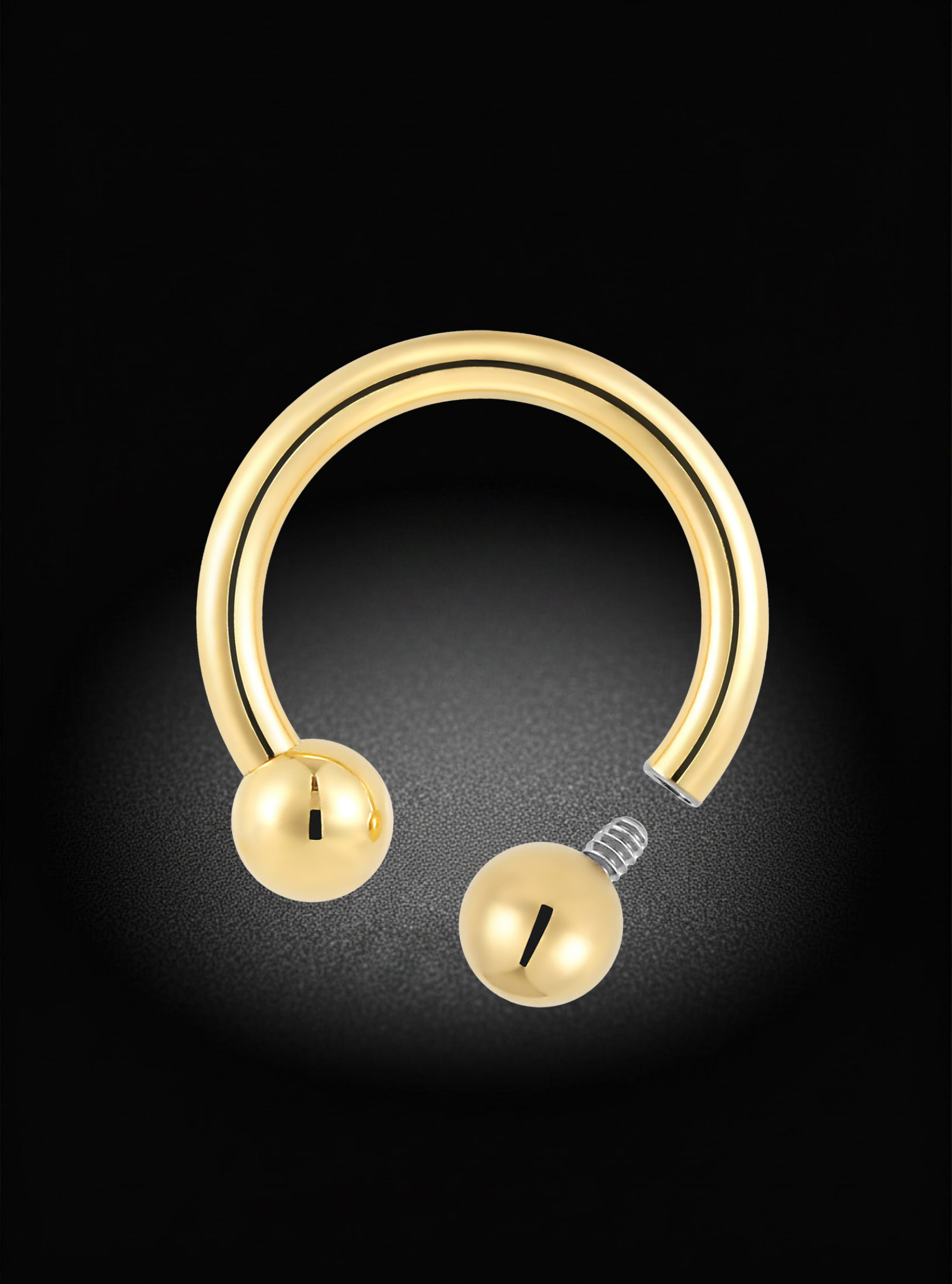 A gold-plated curved hoop piercing stud with two spherical ball ends and a visible screw-back clasp, shown on a black background with a soft spotlight effect.