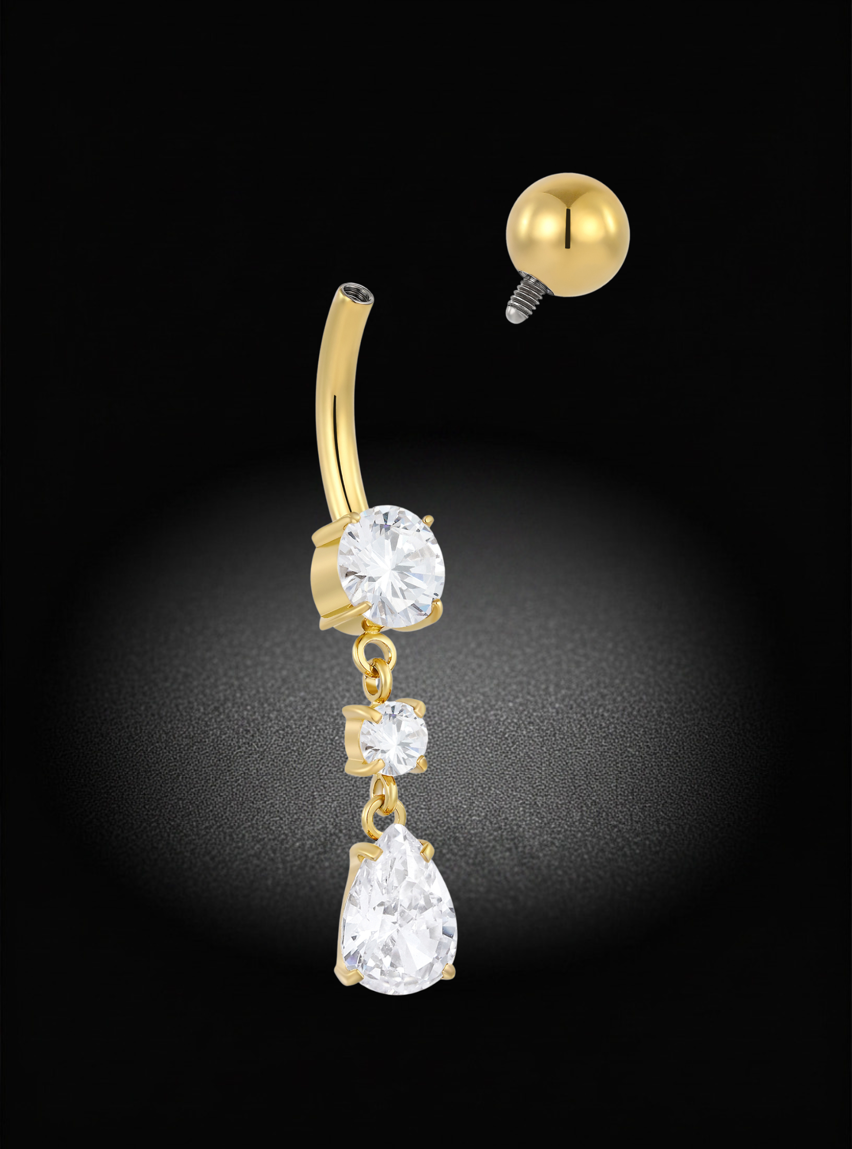 Gold-plated curved barbell belly button piercing with three dangling clear gemstones (oval, square, and teardrop shapes) and a separate ball end piece shown above, set against a black background with a spotlight effect.