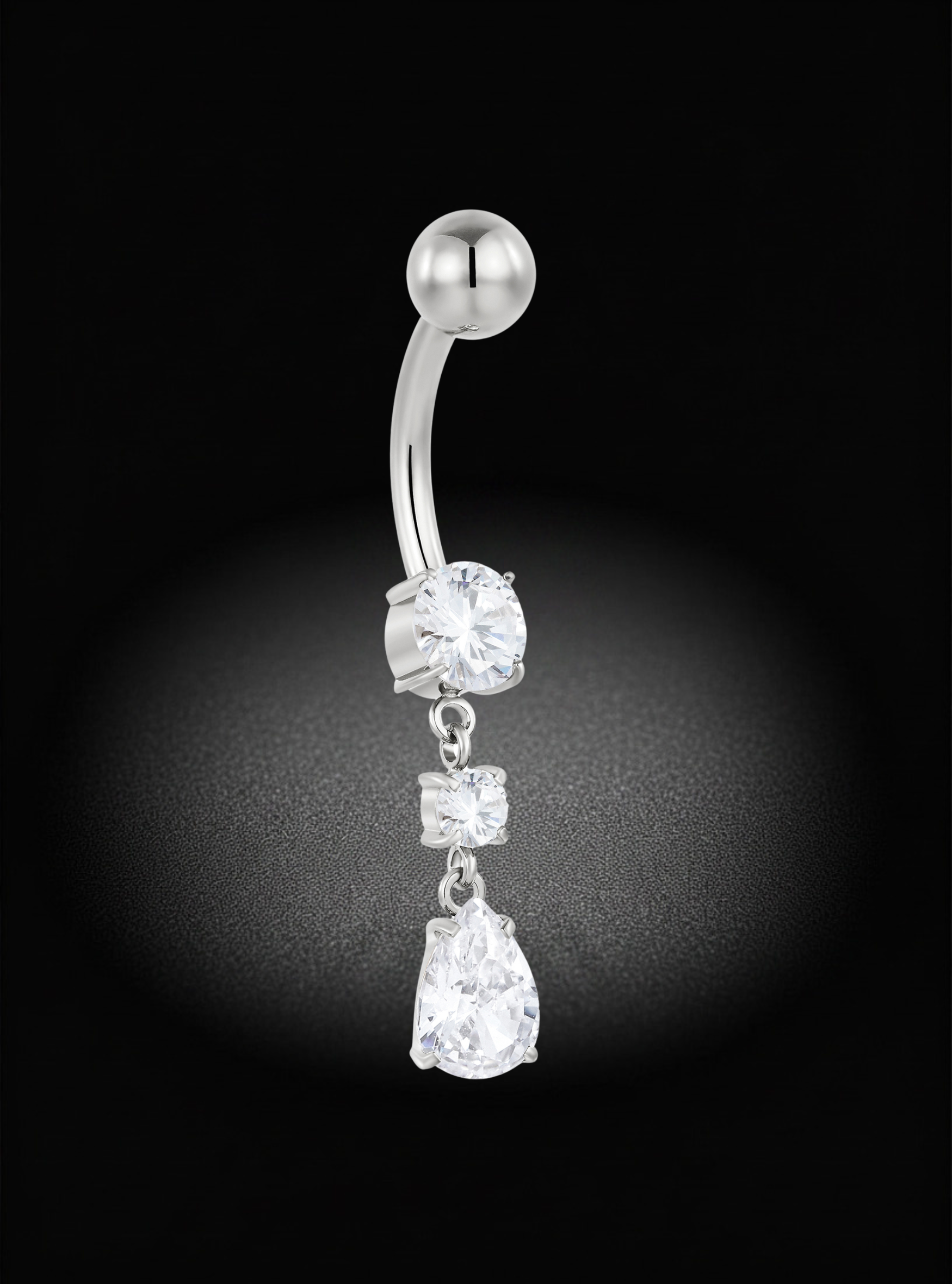 A silver-toned curved barbell belly button ring with three dangling clear gemstones of graduated sizes, set against a black background with a soft spotlight effect.