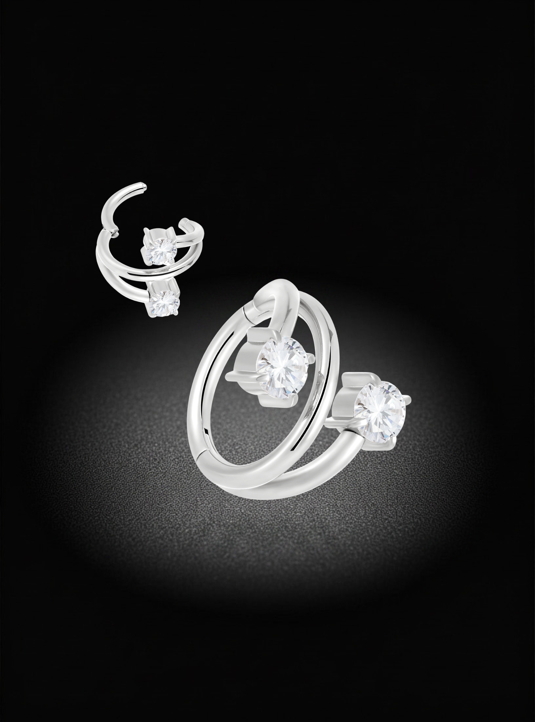 A pair of silver hoop earrings with clear gemstones, displayed on a black background with a spotlight effect.