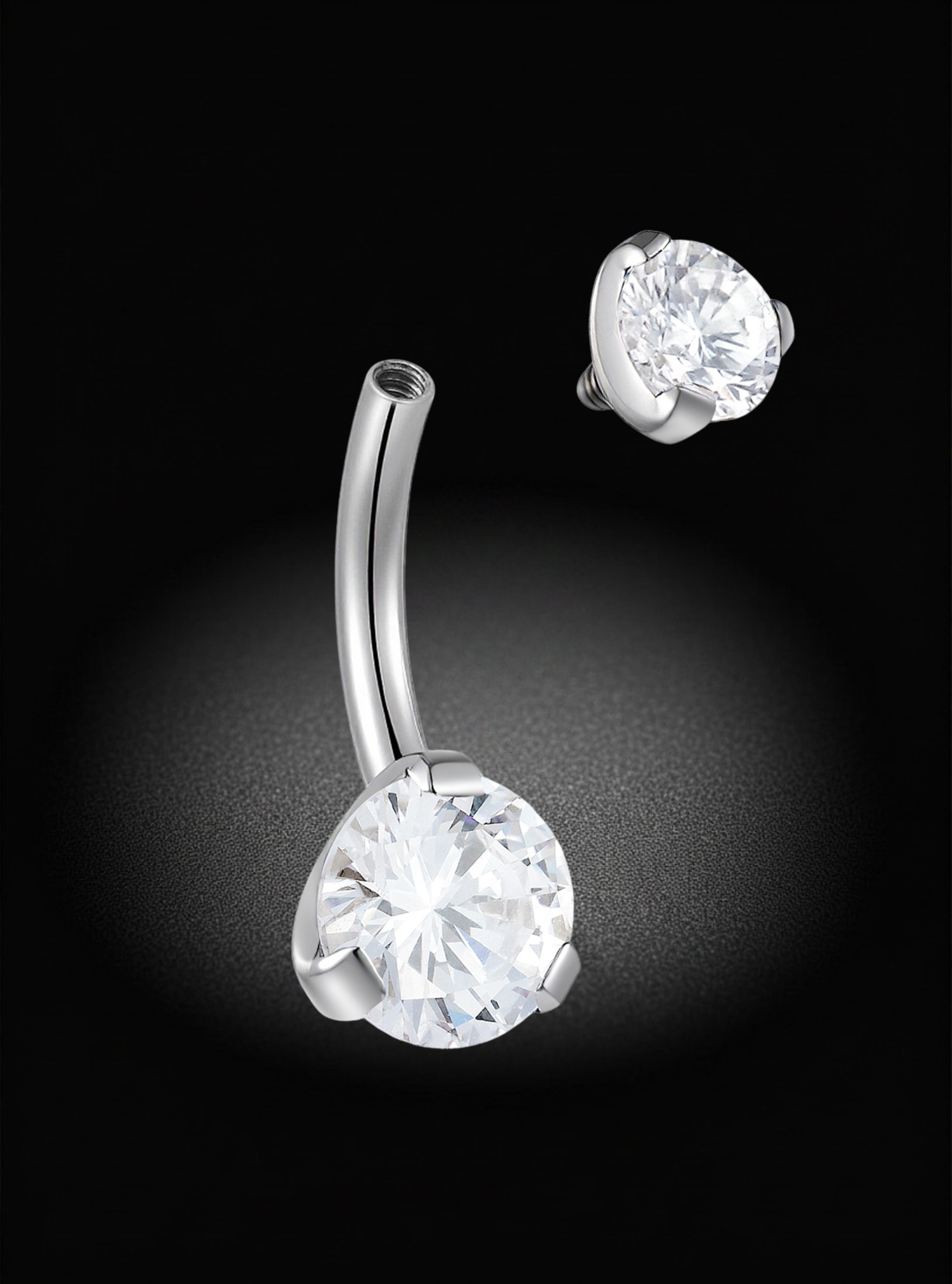 A silver-toned curved barbell belly button piercing with a large clear round-cut gemstone, shown alongside a matching side-view stud on a black background.