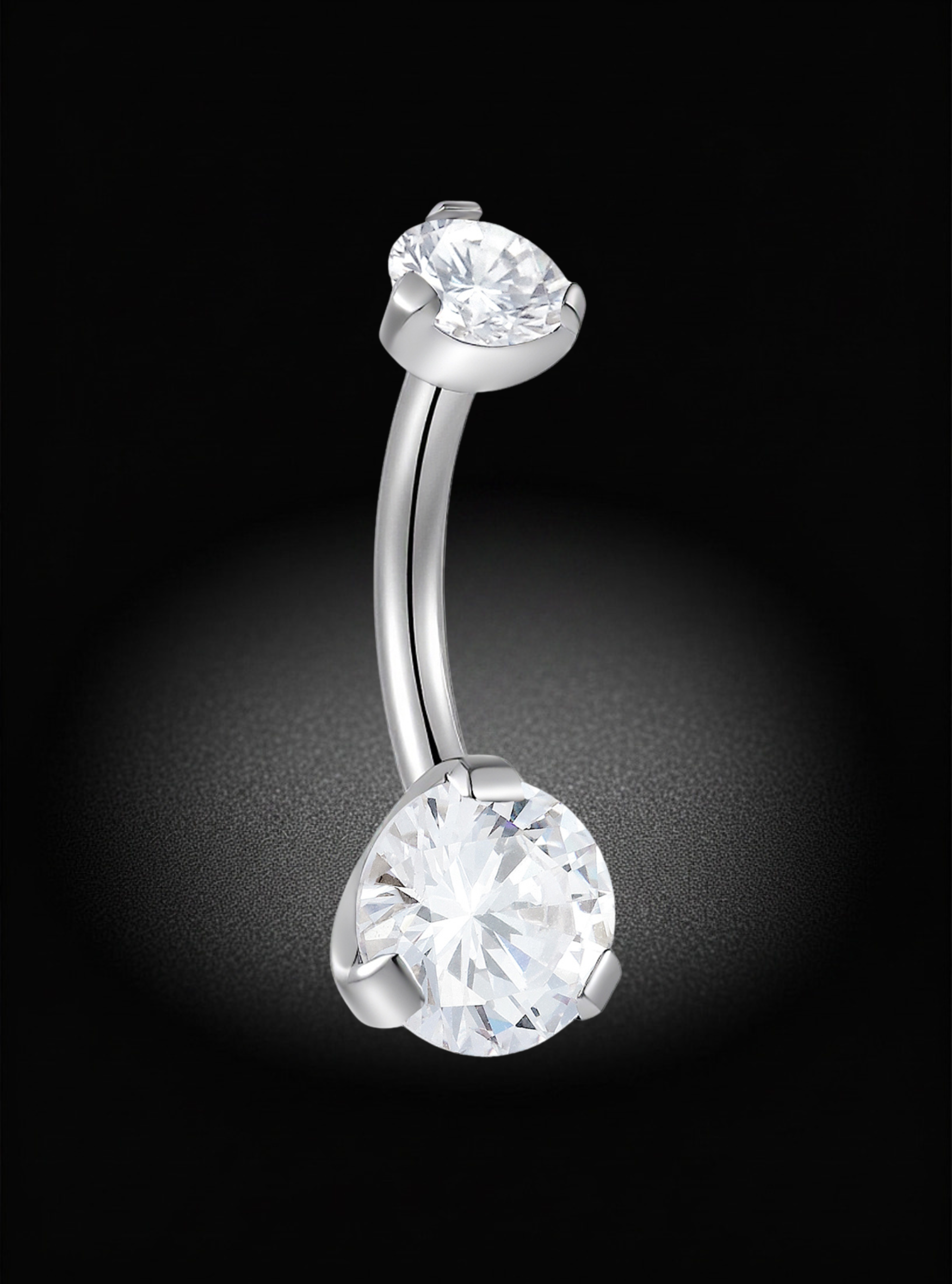 A curved barbell belly button ring with two clear heart-shaped gemstones in a silver-toned setting, photographed against a black background with a soft spotlight effect.