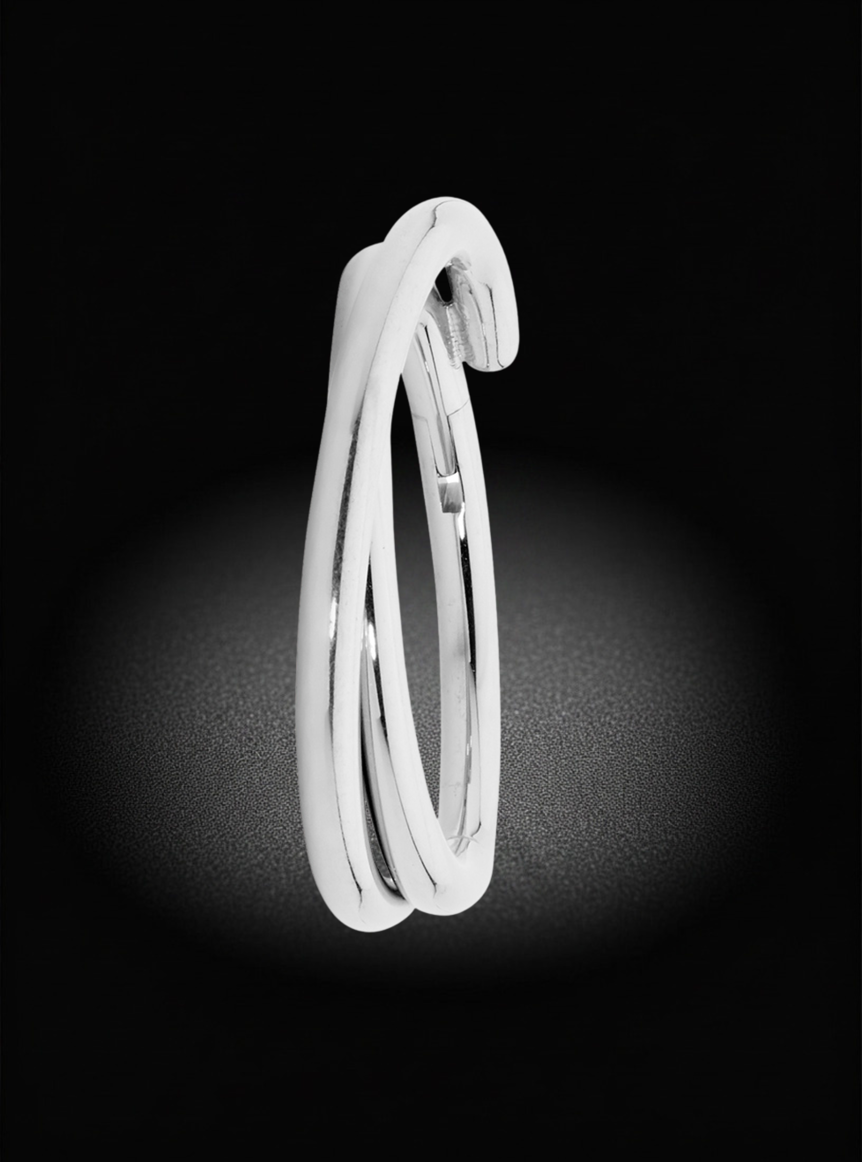 A polished silver-toned wrap-around ring or bangle shown alone on a black background with a soft spotlight effect.