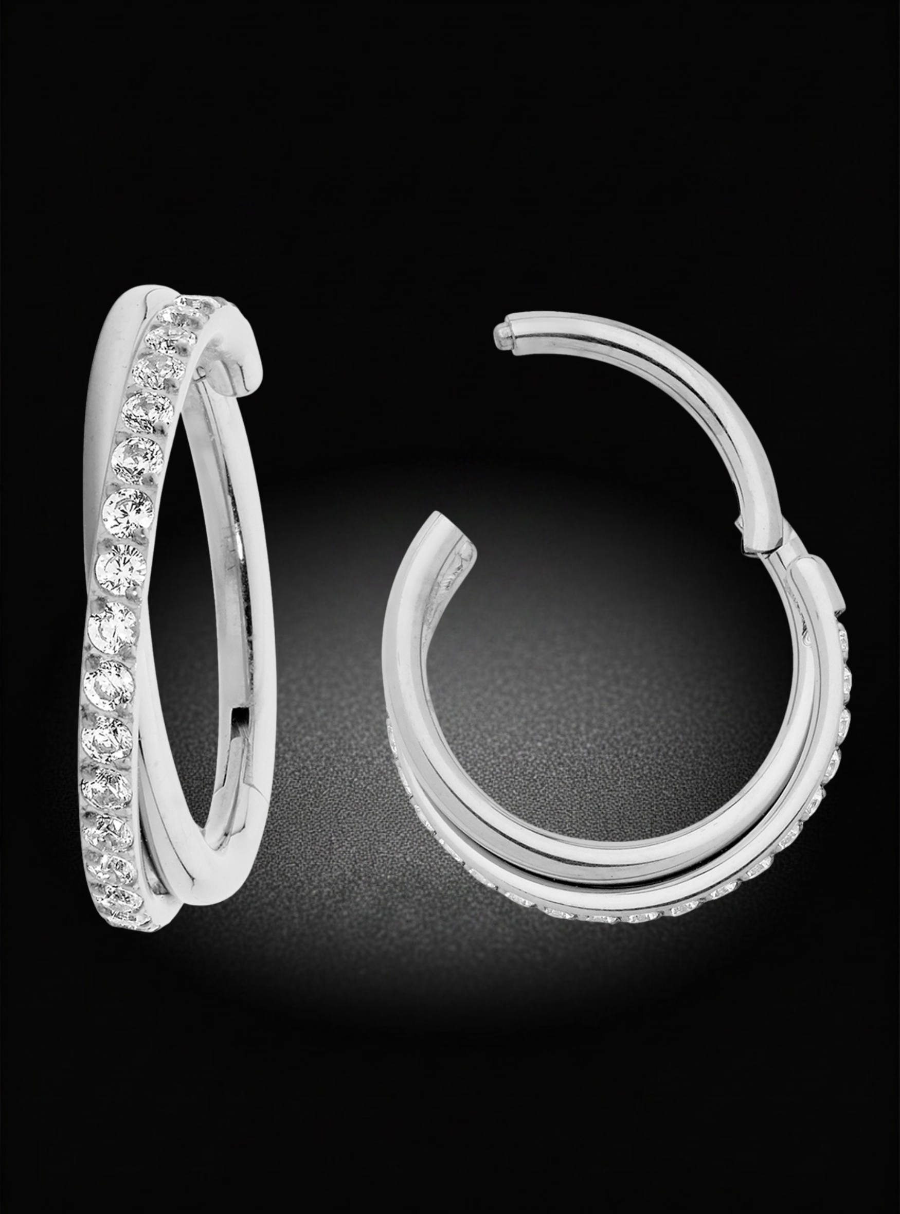 A pair of polished silver hoop earrings, one featuring a channel-set row of clear stones and the other showing a textured outer edge, set against a dark black background.