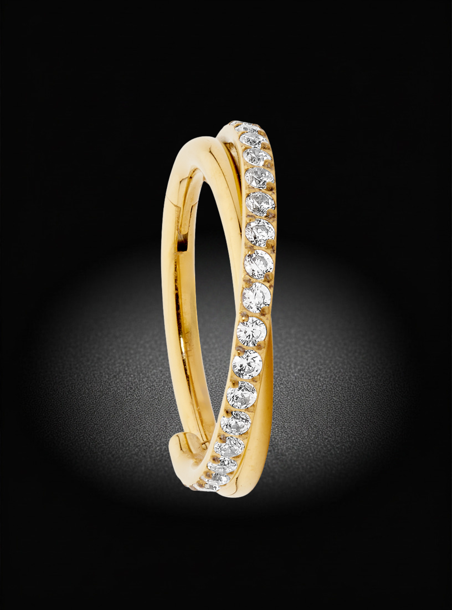 A gold huggie ring featuring a channel-set row of clear round diamonds on one side, shown against a dark black background with a soft spotlight effect.