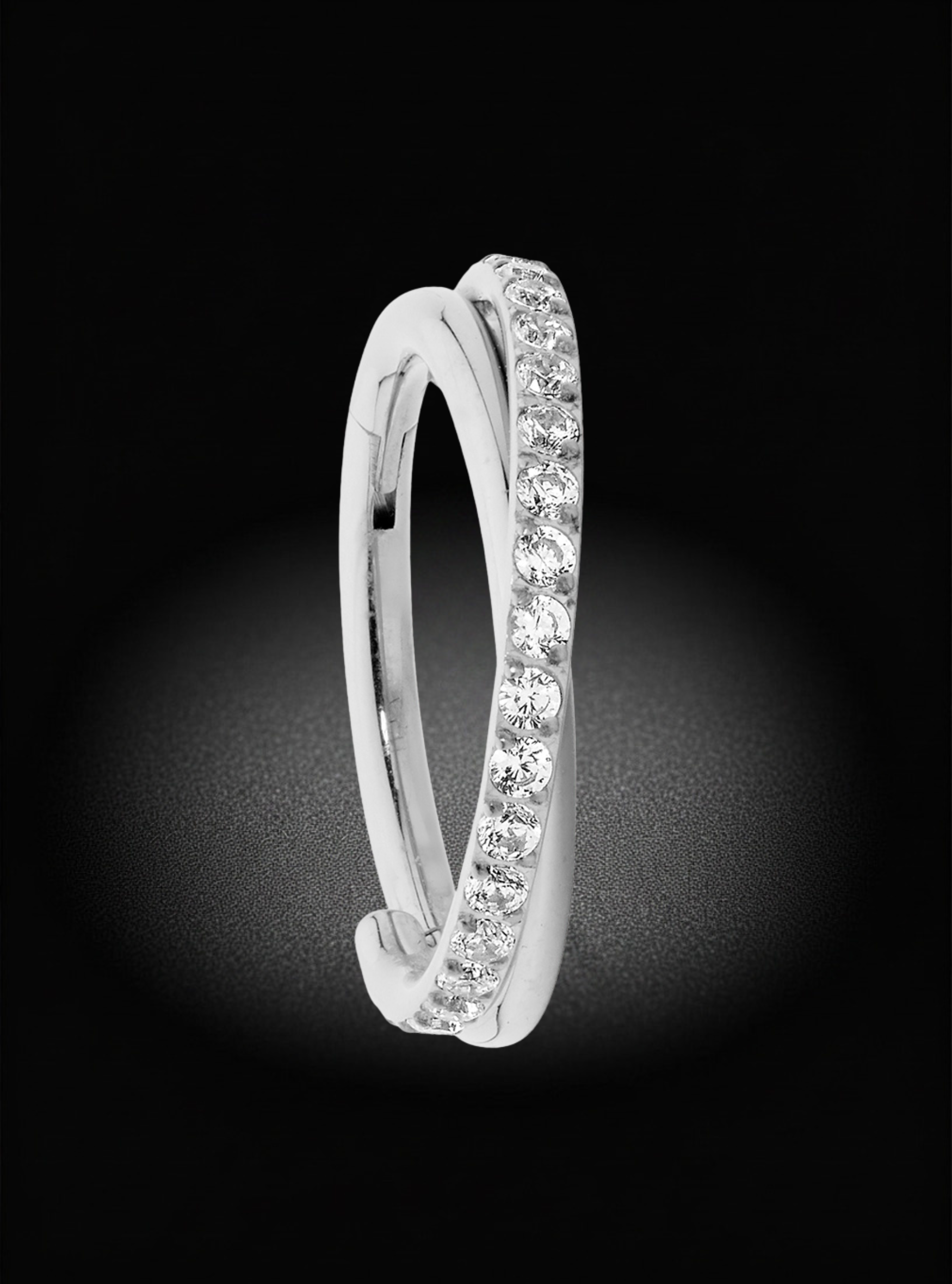 A silver-tone double-band ring with a row of clear pavé-set stones on the outer band, shown against a dark black background with a soft spotlight effect.