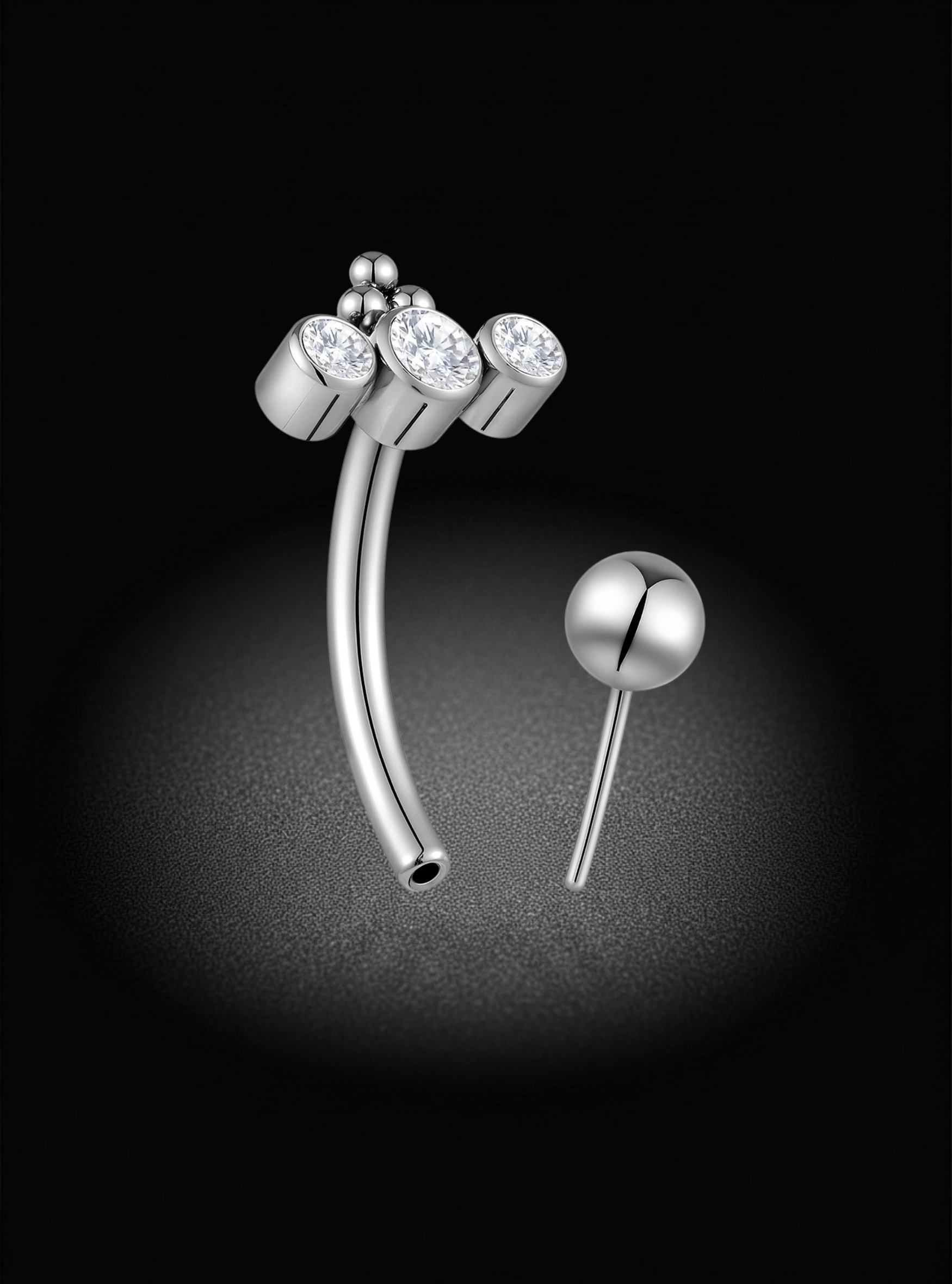 Silver curved titanium eyebrow barbell body jewelry with three clear gemstone clusters on one end and a polished ball stud on the other, displayed on a black background.