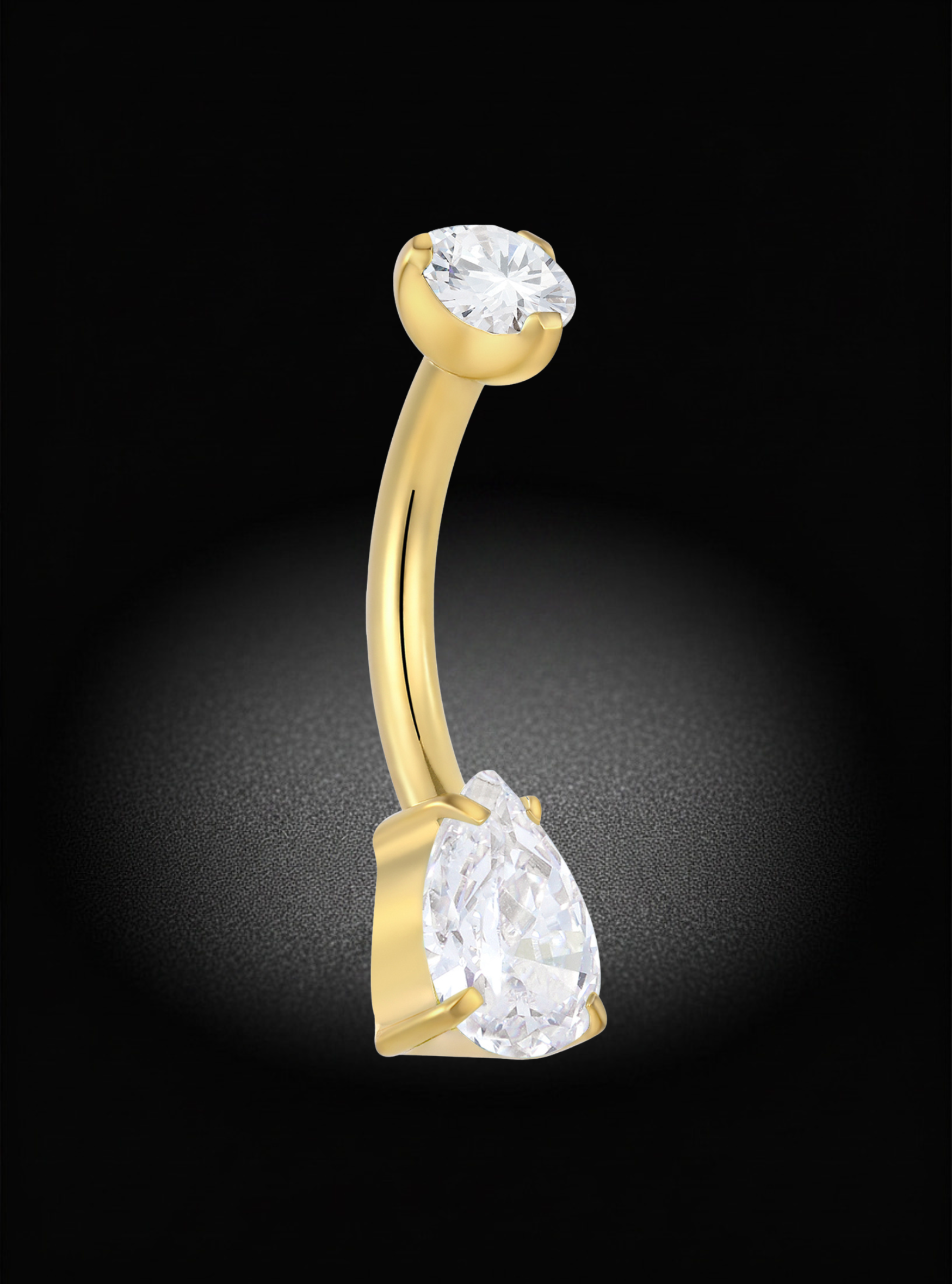 A curved gold barbell belly button ring featuring a large pear-cut clear gemstone at the bottom and a smaller oval-cut clear gemstone at the top, set against a dark background with a spotlight effect.