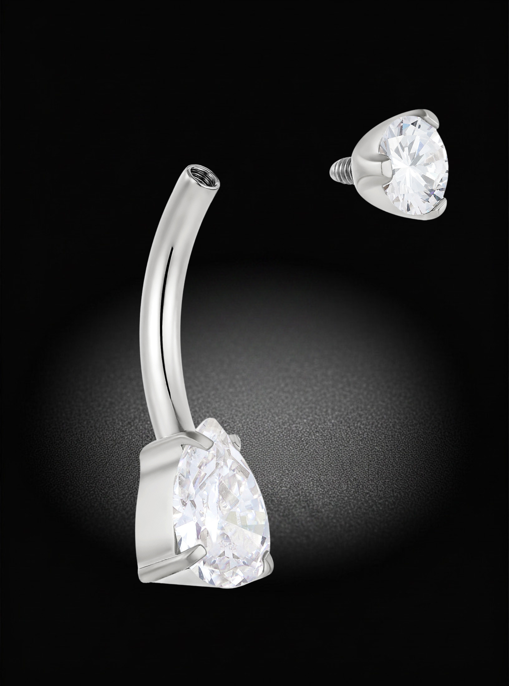 A silver-toned curved barbell belly button piercing with a large clear teardrop gemstone, shown alongside a matching close-up of the stone and backing on a black background.