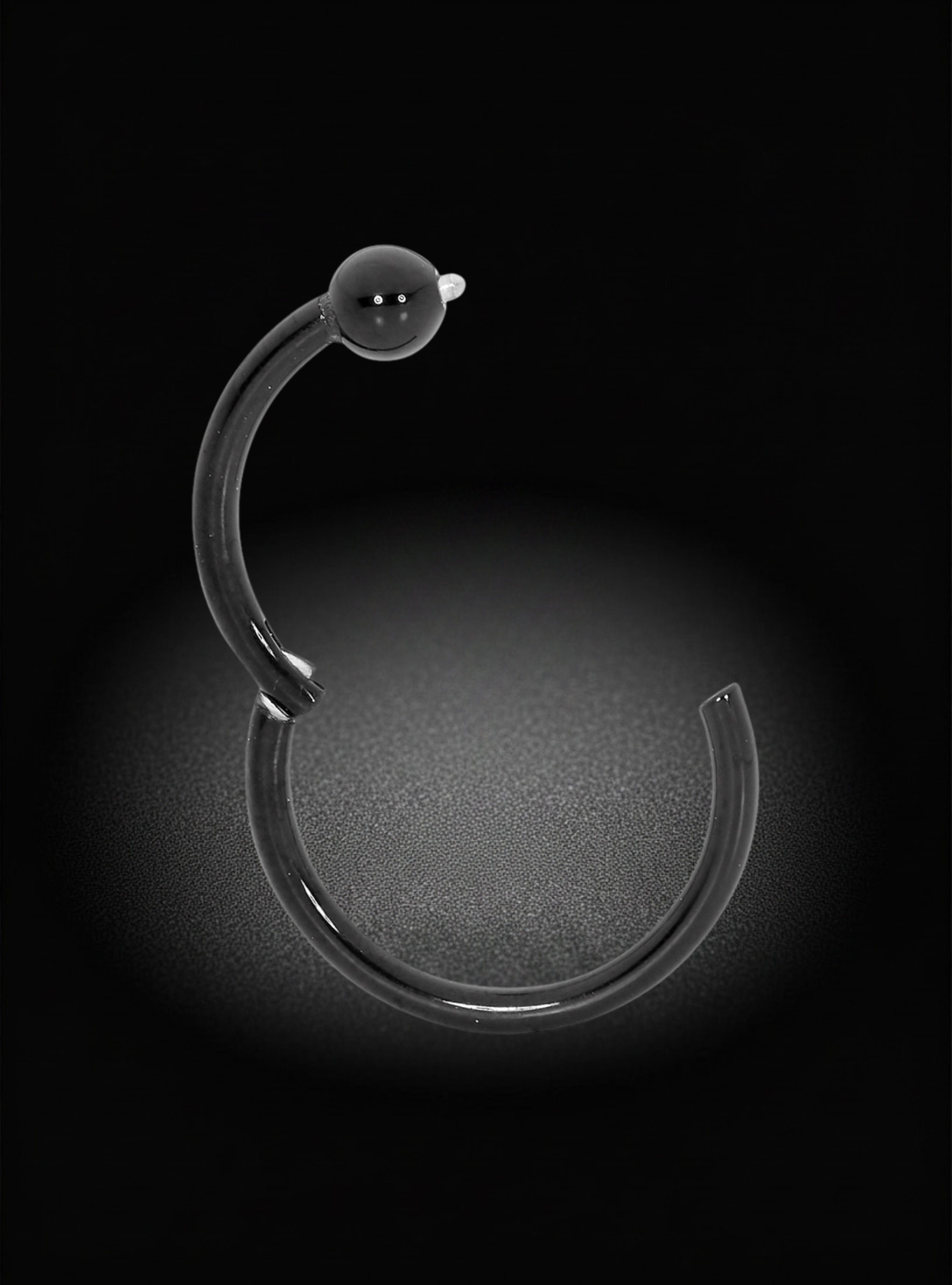 A black titanium hinged segment ring ball closure earring with a spherical bead detail at the top, displayed against a dark background with a soft spotlight effect.