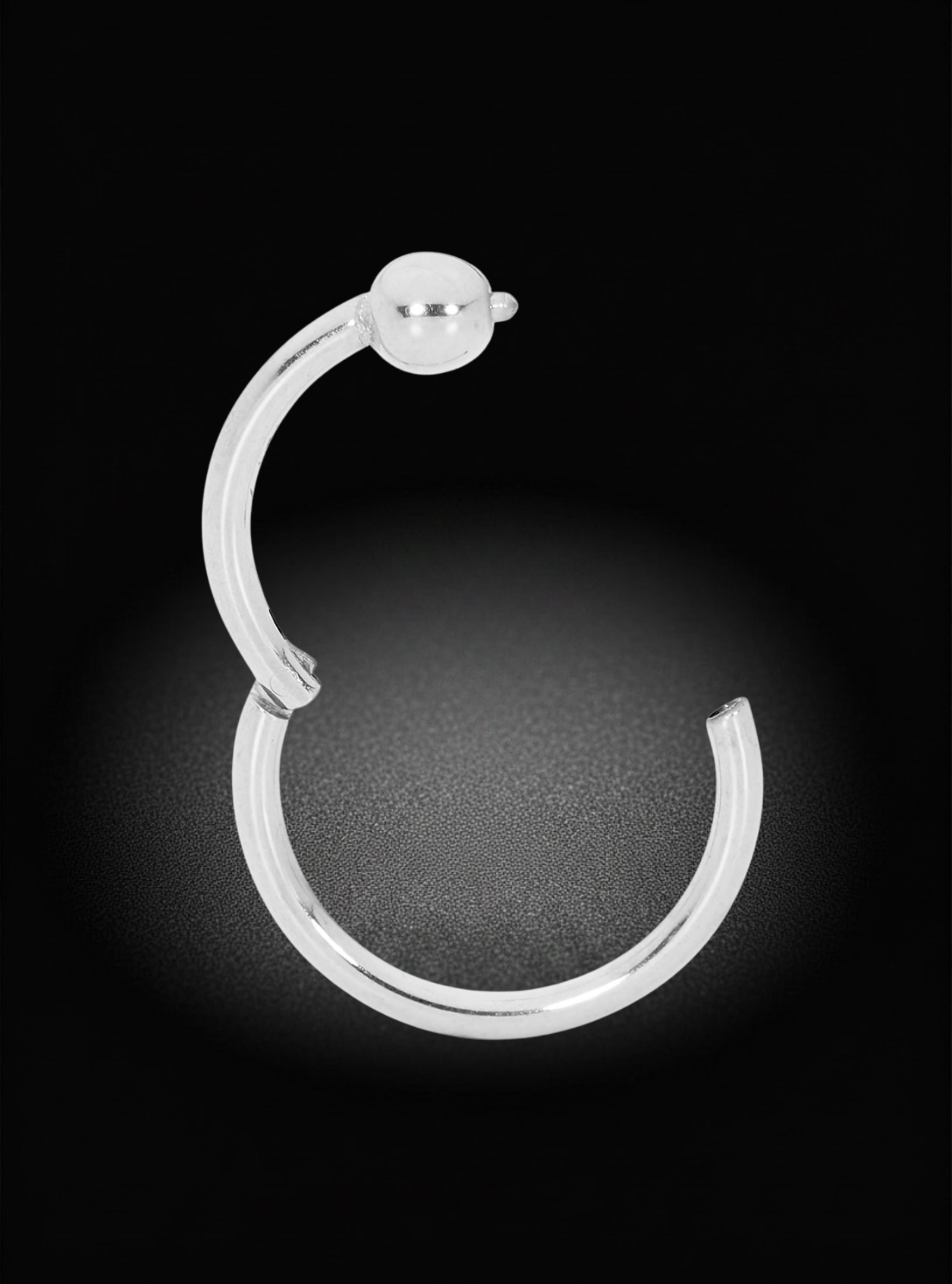 A polished silver-toned curved hoop earring with a small spherical bead detail at the top, shown against a dark black background with a soft spotlight effect.