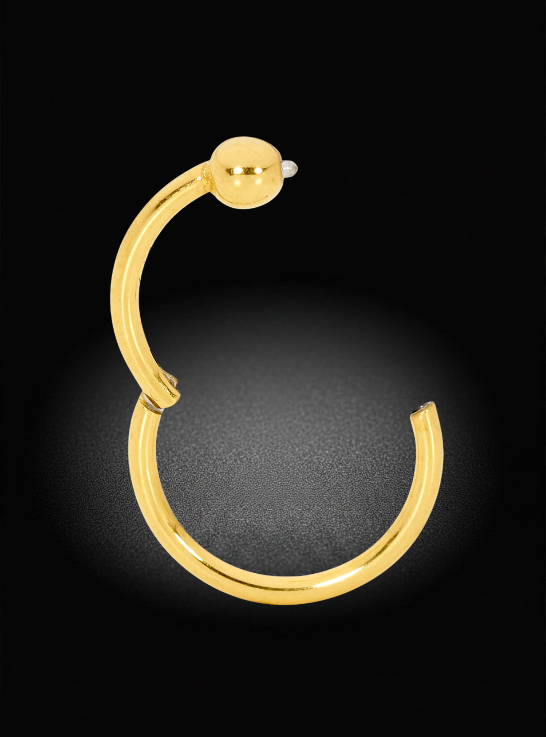 A single gold hoop earring with a small spherical bead detail at the top, shown on a black background with a soft spotlight effect.