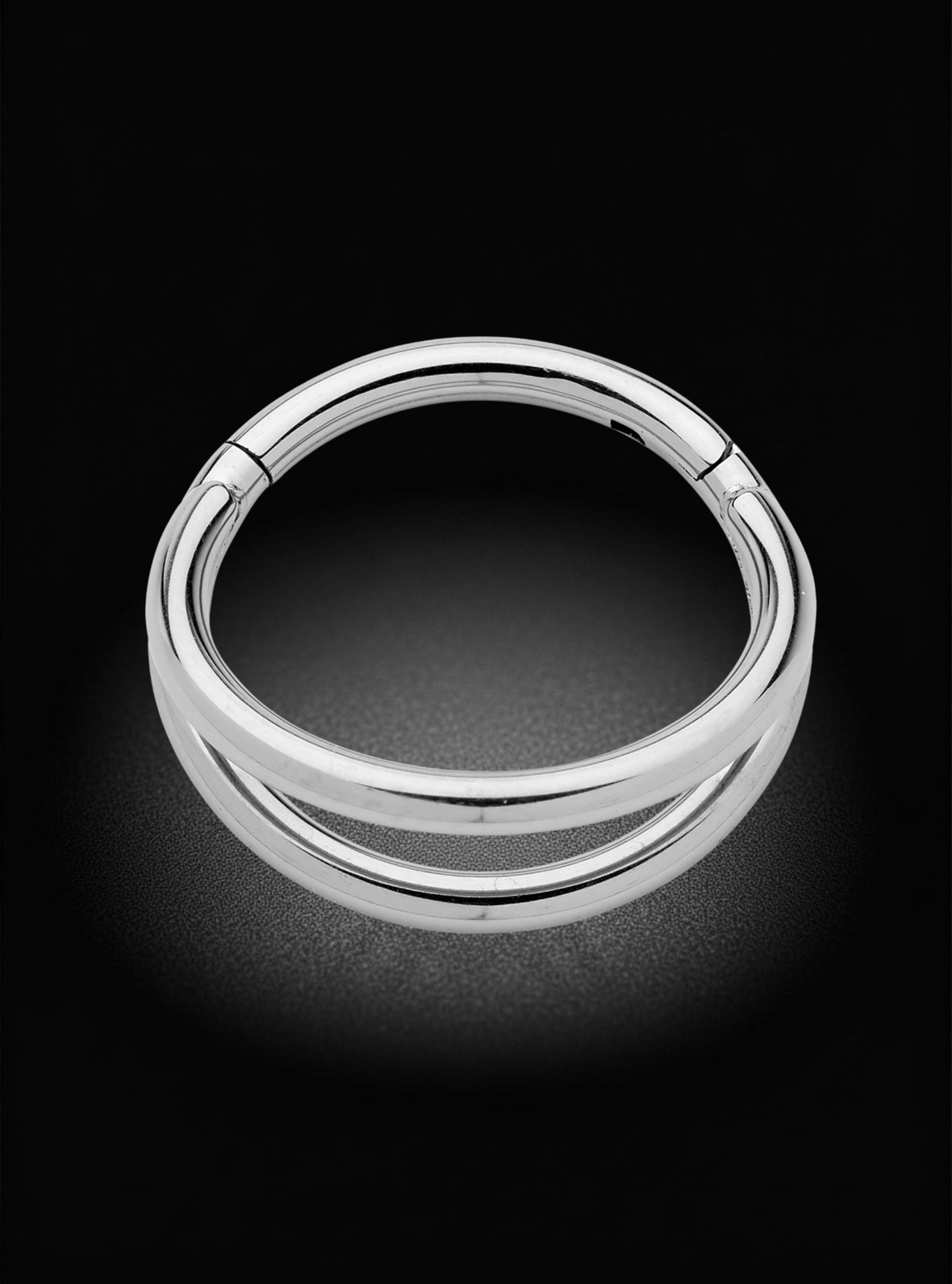 A polished silver-toned metal ring with a double-band design, photographed against a dark black background with a soft glow.