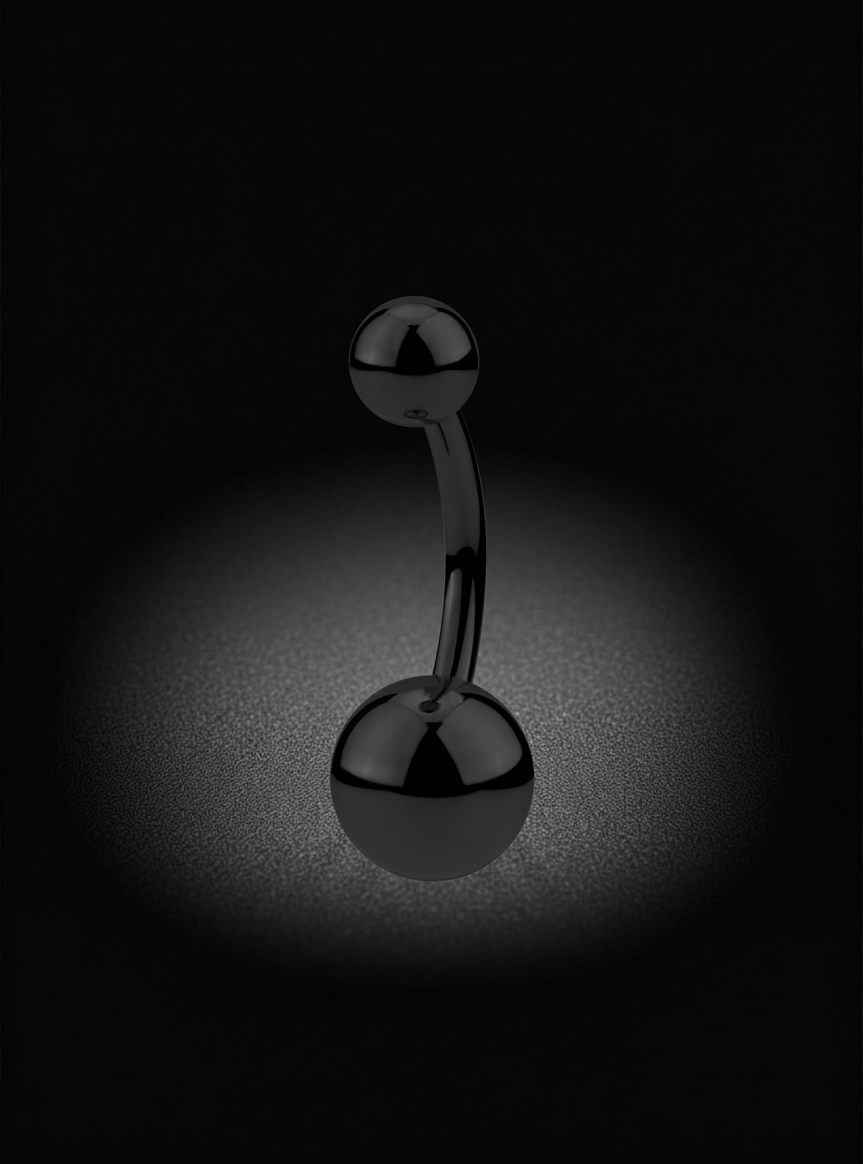 A curved belly barbell-style body jewelry piece with two polished black spherical ends, photographed against a dark background with a soft spotlight around the base.