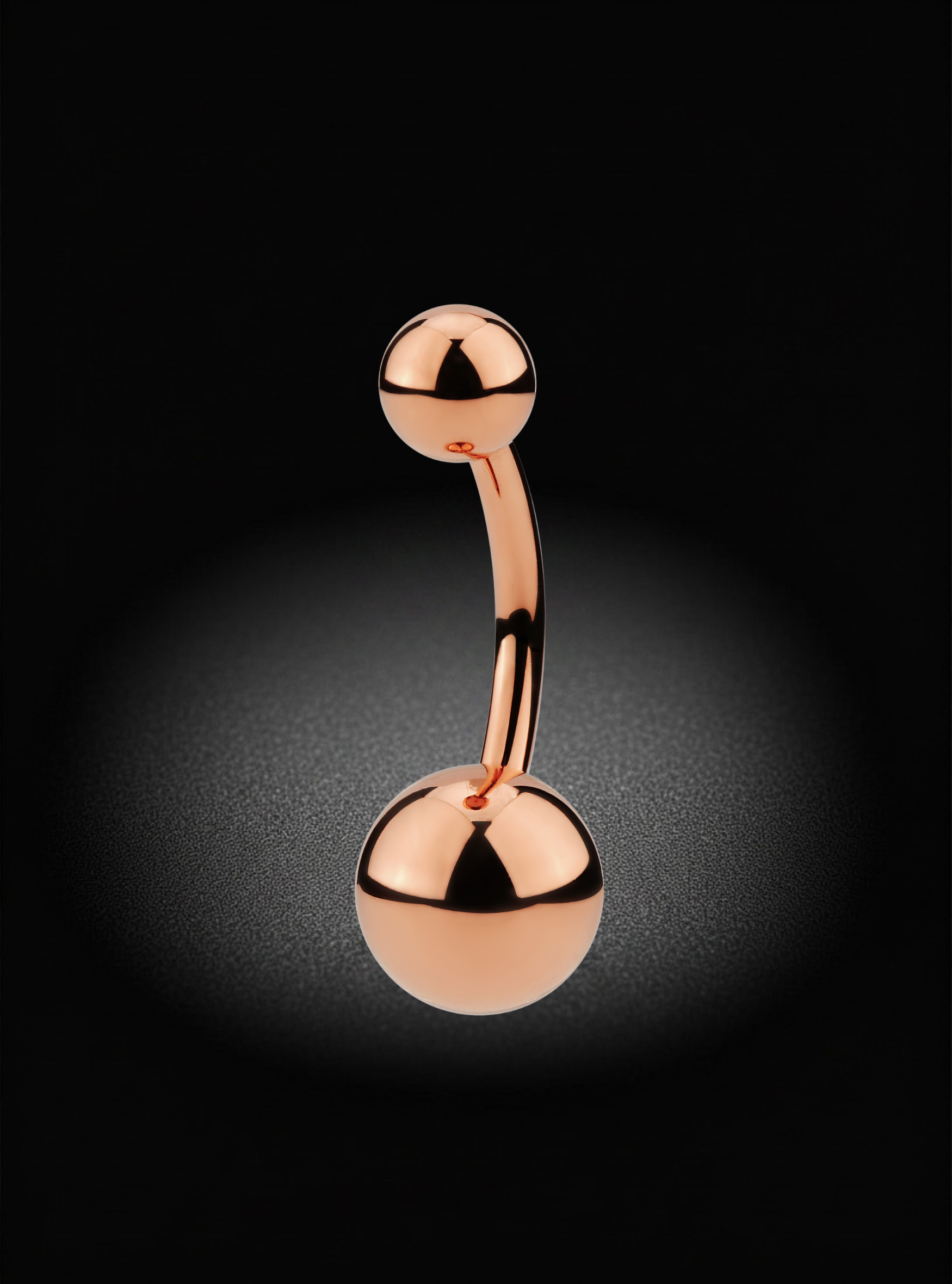 A rose gold curved barbell belly button piercing with spherical ends, shown on a dark background with a spotlight effect.