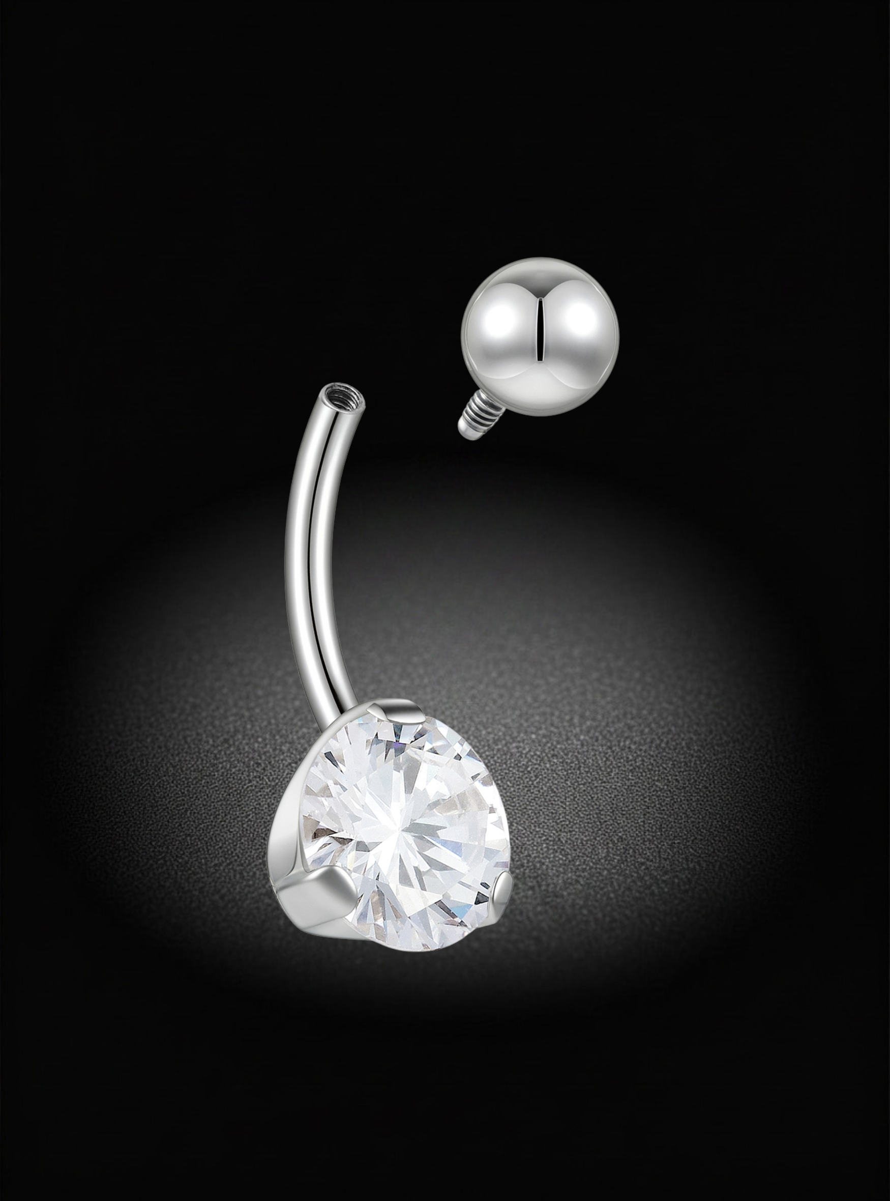 A silver-toned curved barbell belly button ring with a large clear faceted heart-shaped gemstone and a matching round silver ball stud, shown on a black background with a spotlight effect.