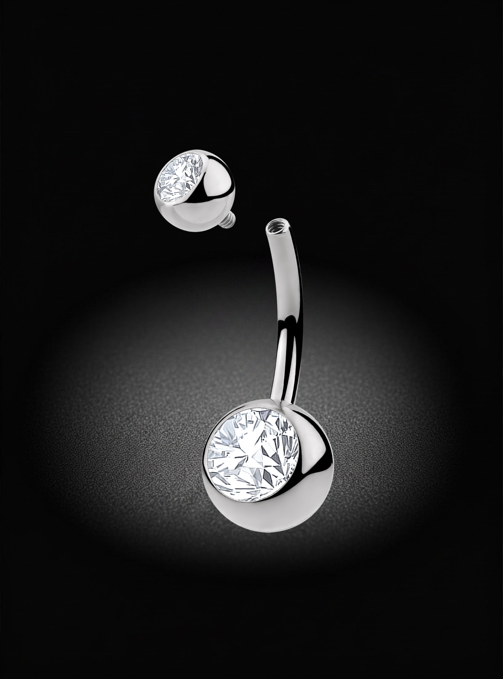 A silver-toned curved barbell belly button ring with a large round clear gemstone on the ball end, shown floating against a black background with a soft spotlight effect.