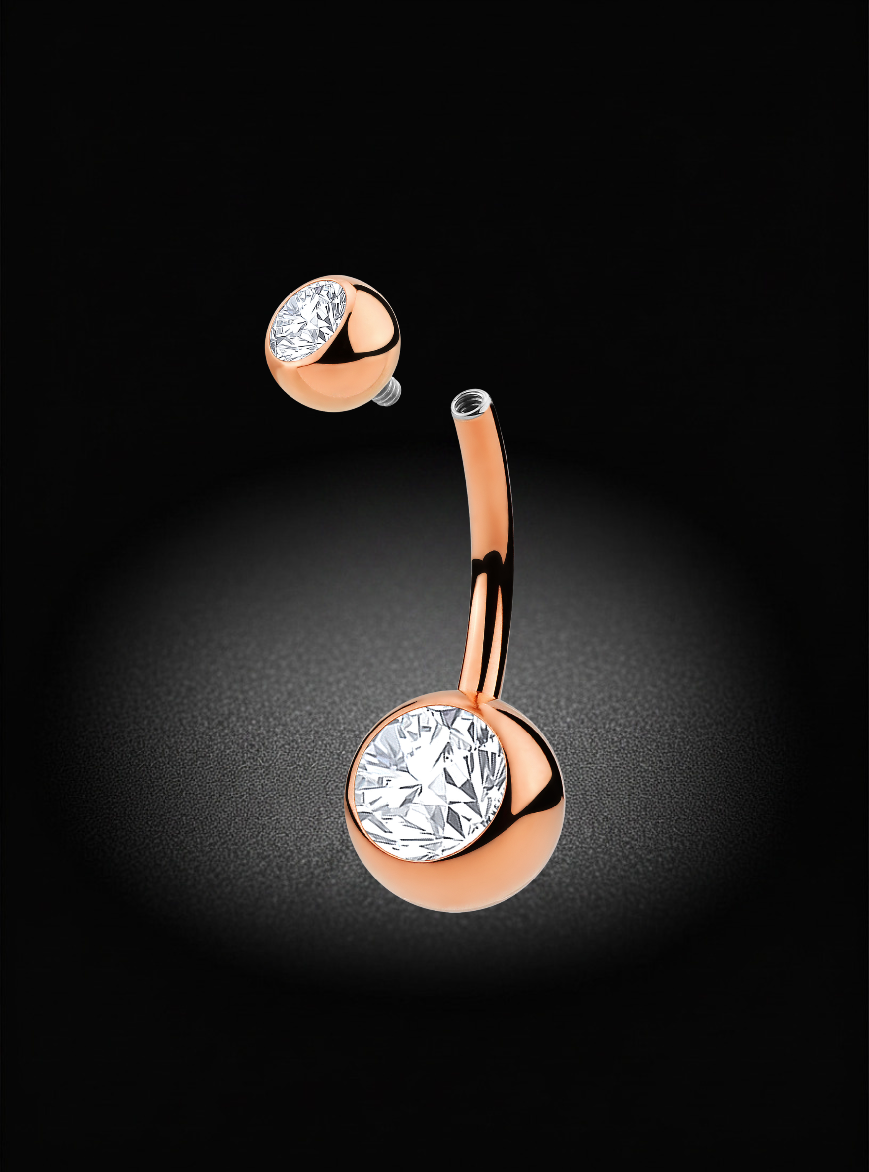 A rose gold curved barbell belly button piercing with a large round bezel-set clear gemstone on the flat end, shown floating against a dark black background with a soft spotlight effect.