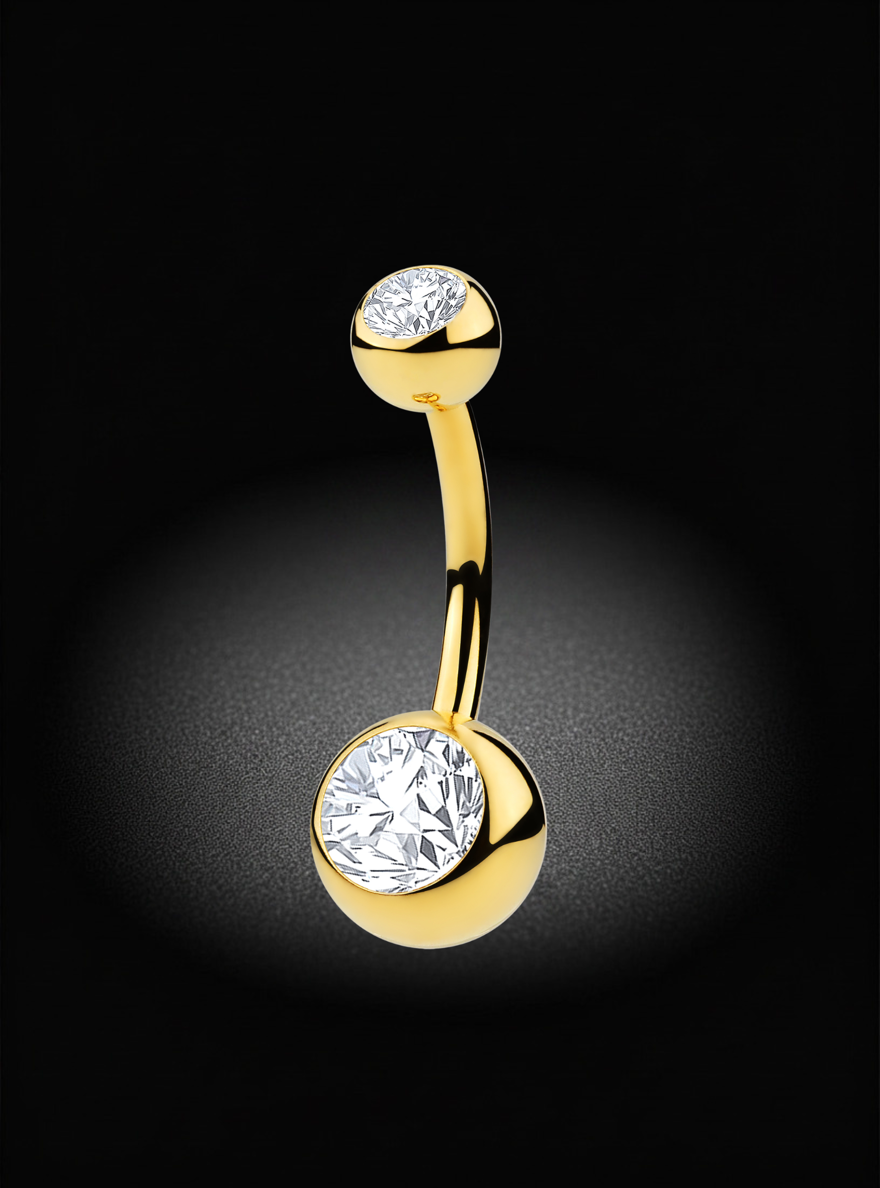 A curved gold-tone belly button ring with two round bezel-set clear gemstones, one at each end, shown on a black background with a soft spotlight effect.